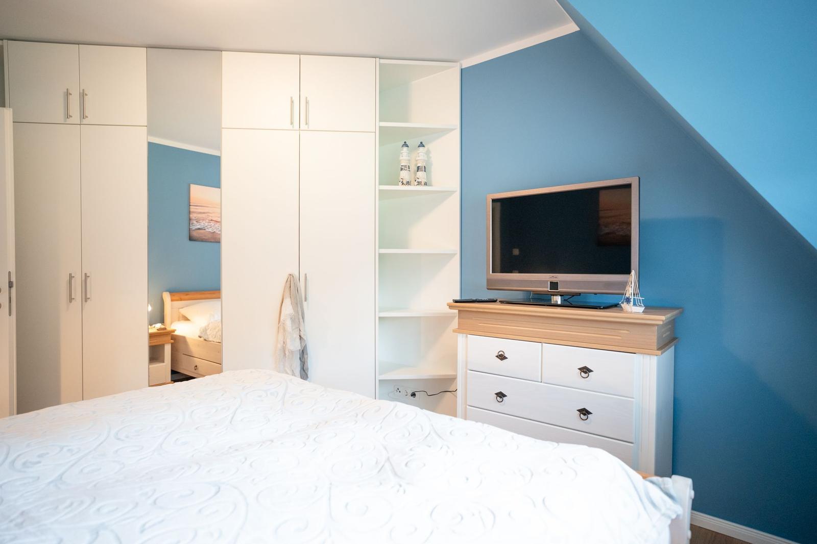 Schlafzimmer mit Doppelbett, Kleiderschrank und Fernseher auf Kommode.