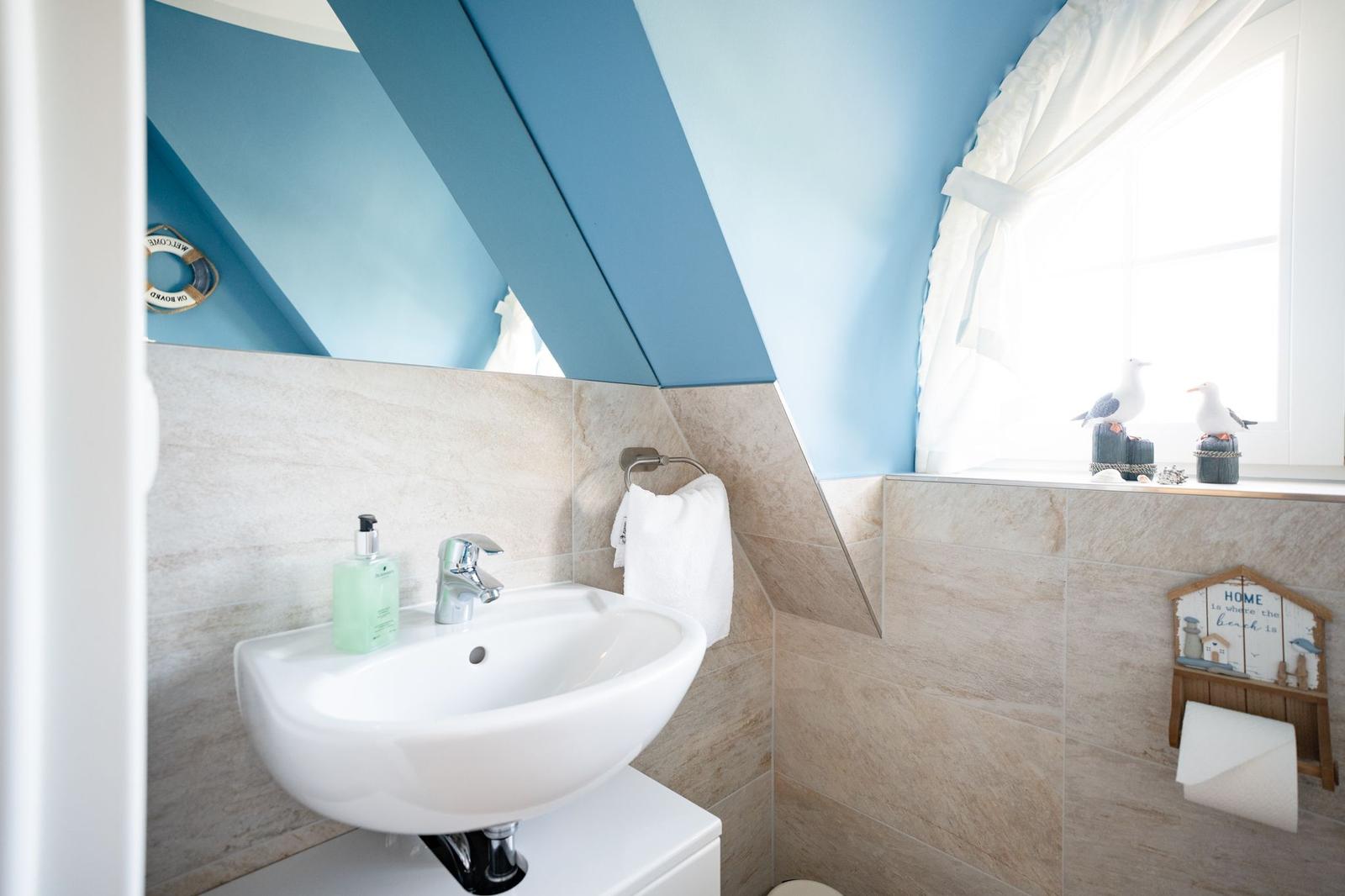 Badezimmer mit Waschbecken, Spiegel und Fenster mit Vogeldekoration.