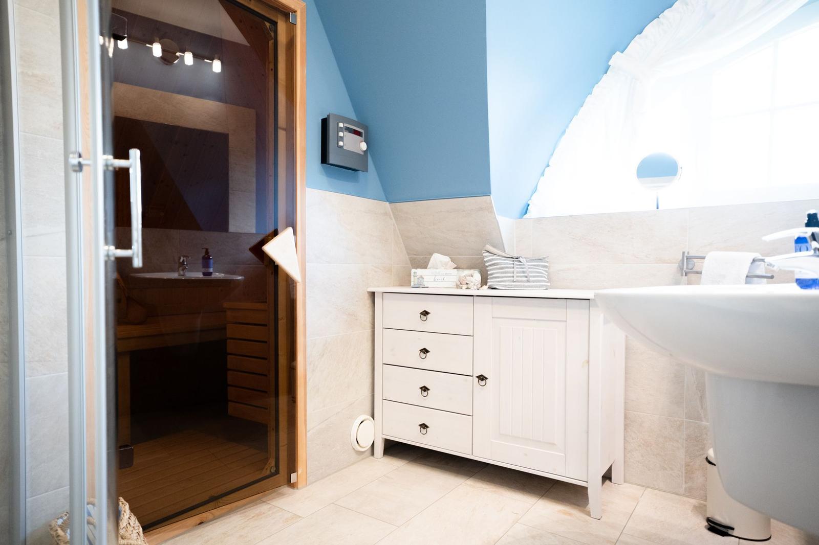 Badezimmer mit Dusche, Waschbecken und Holzsauna