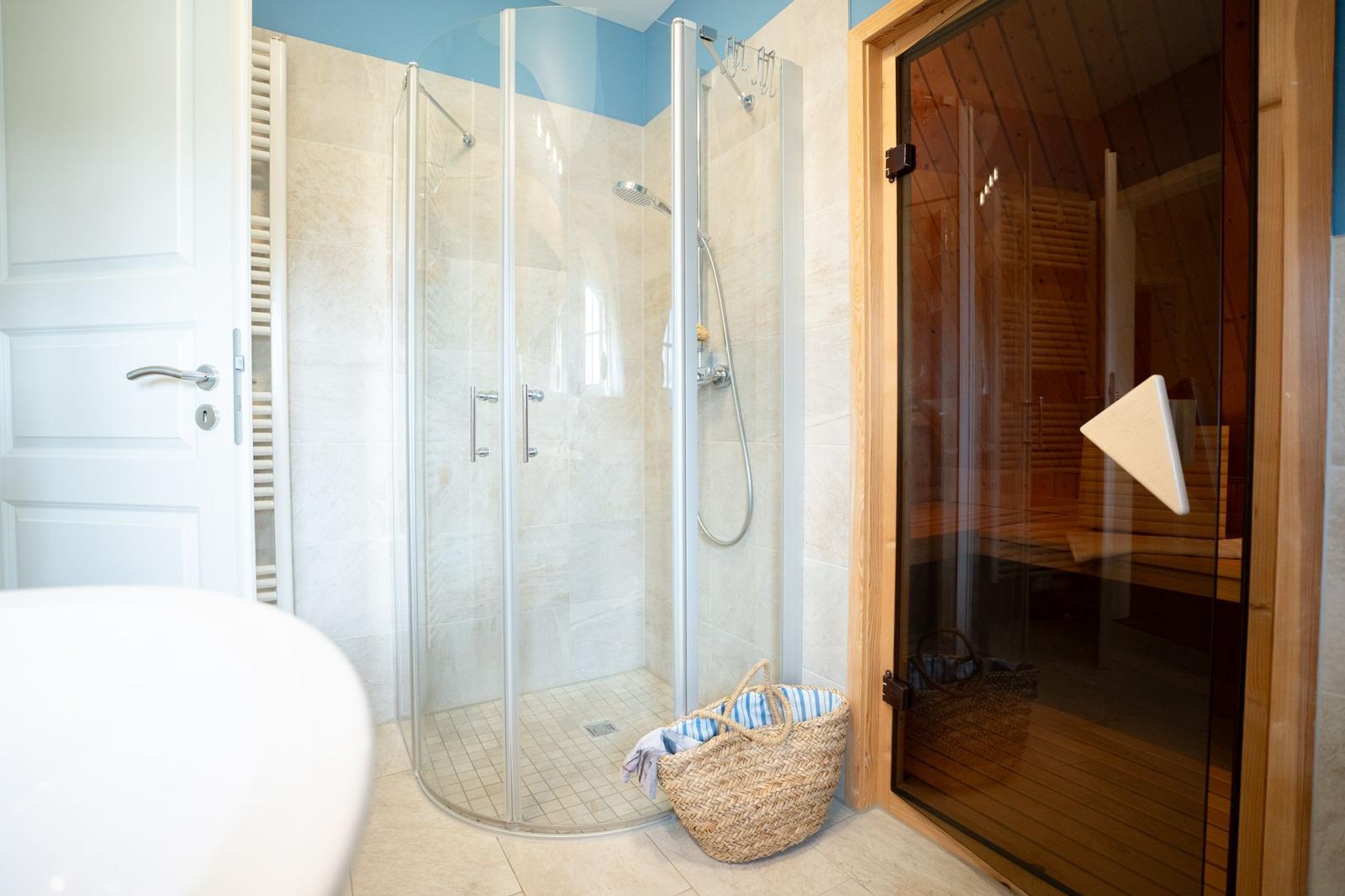 Dusche mit Glaswand und Sauna mit Holztüren.