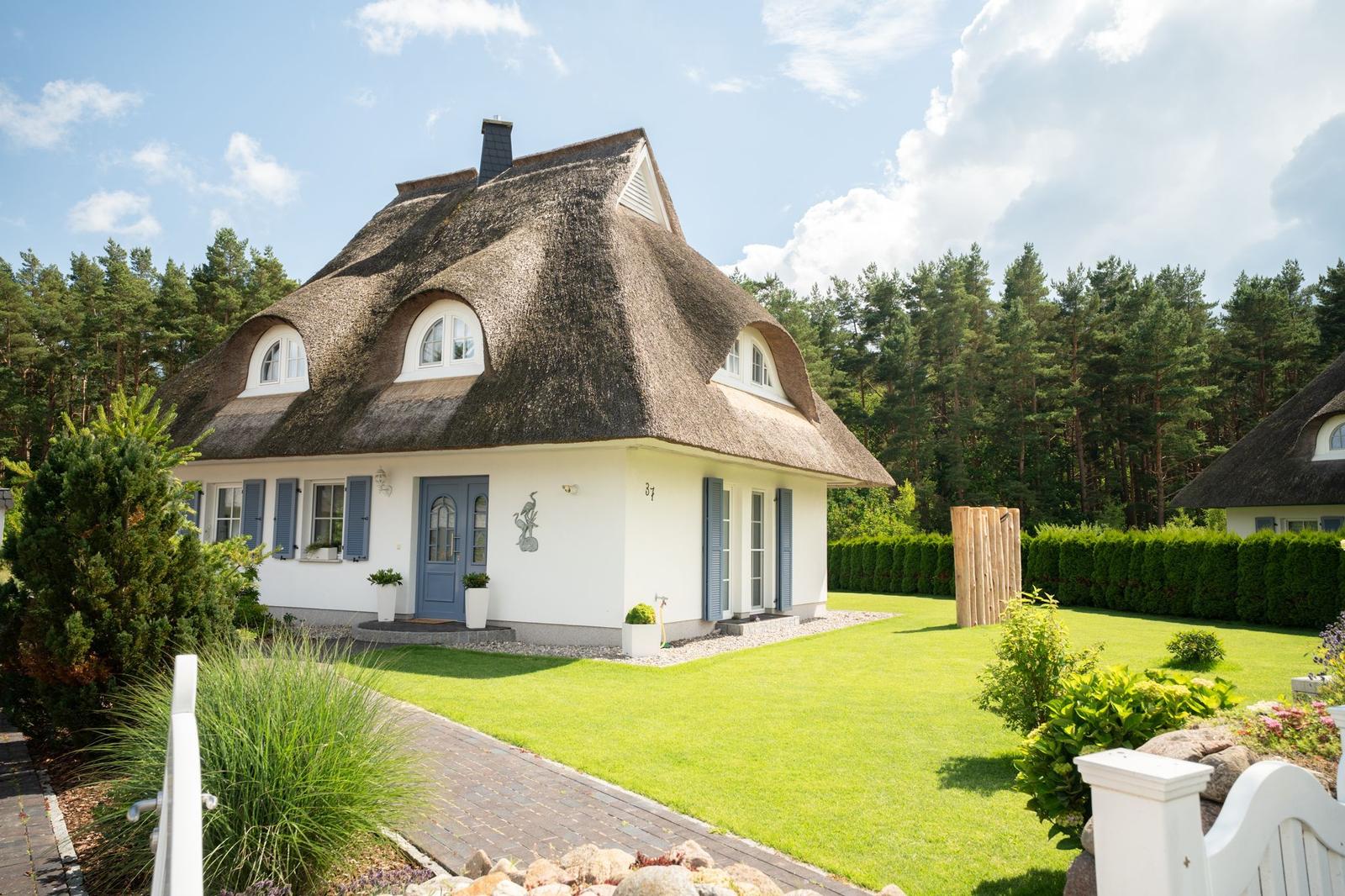 Haus mit Strohdach, blauer Tür und grünem Garten vor Wald.