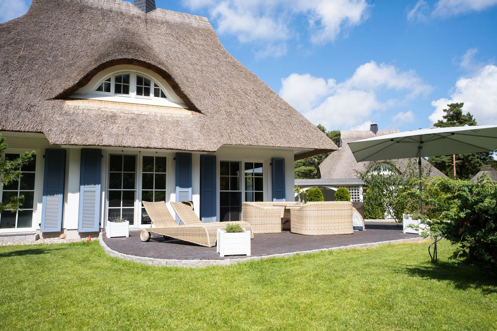 Haus mit Strohdach und Terrasse mit Liegen und Sitzgruppe.