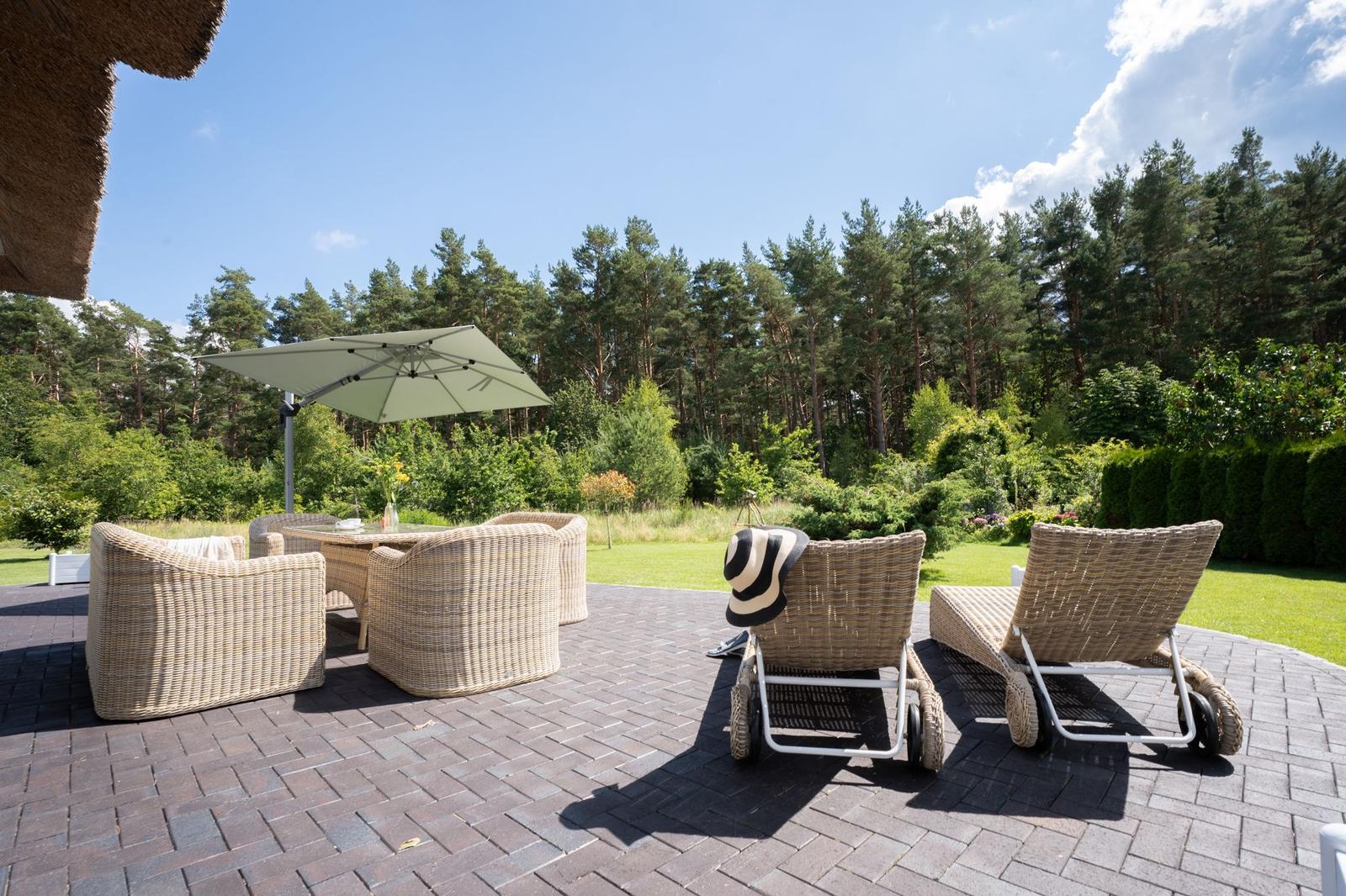Terrasse mit Rattanmöbeln, Sonnenschirm und Blick in den Wald.