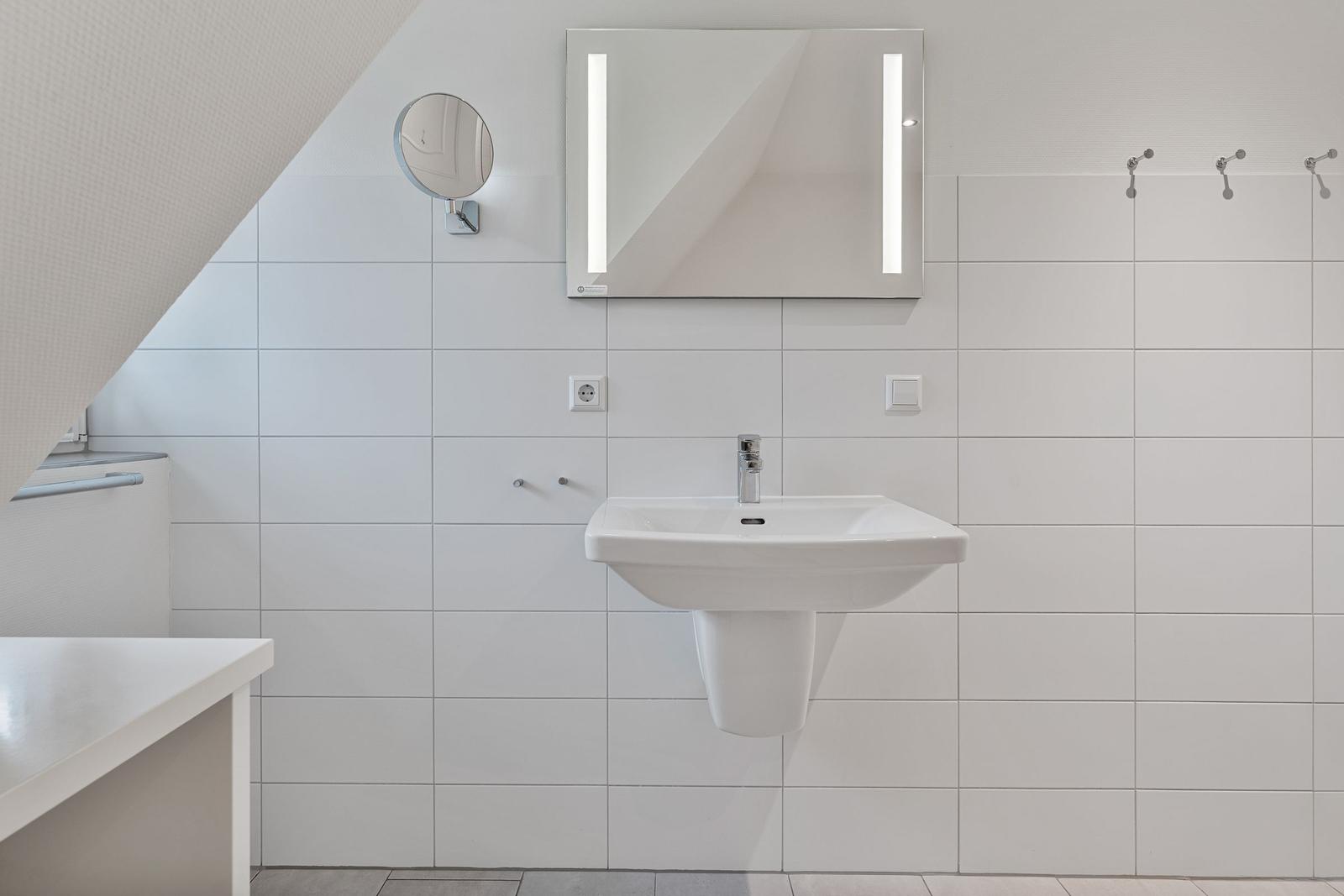 Badezimmer mit Waschbecken, beleuchtetem Spiegel und Haken an der Wand.