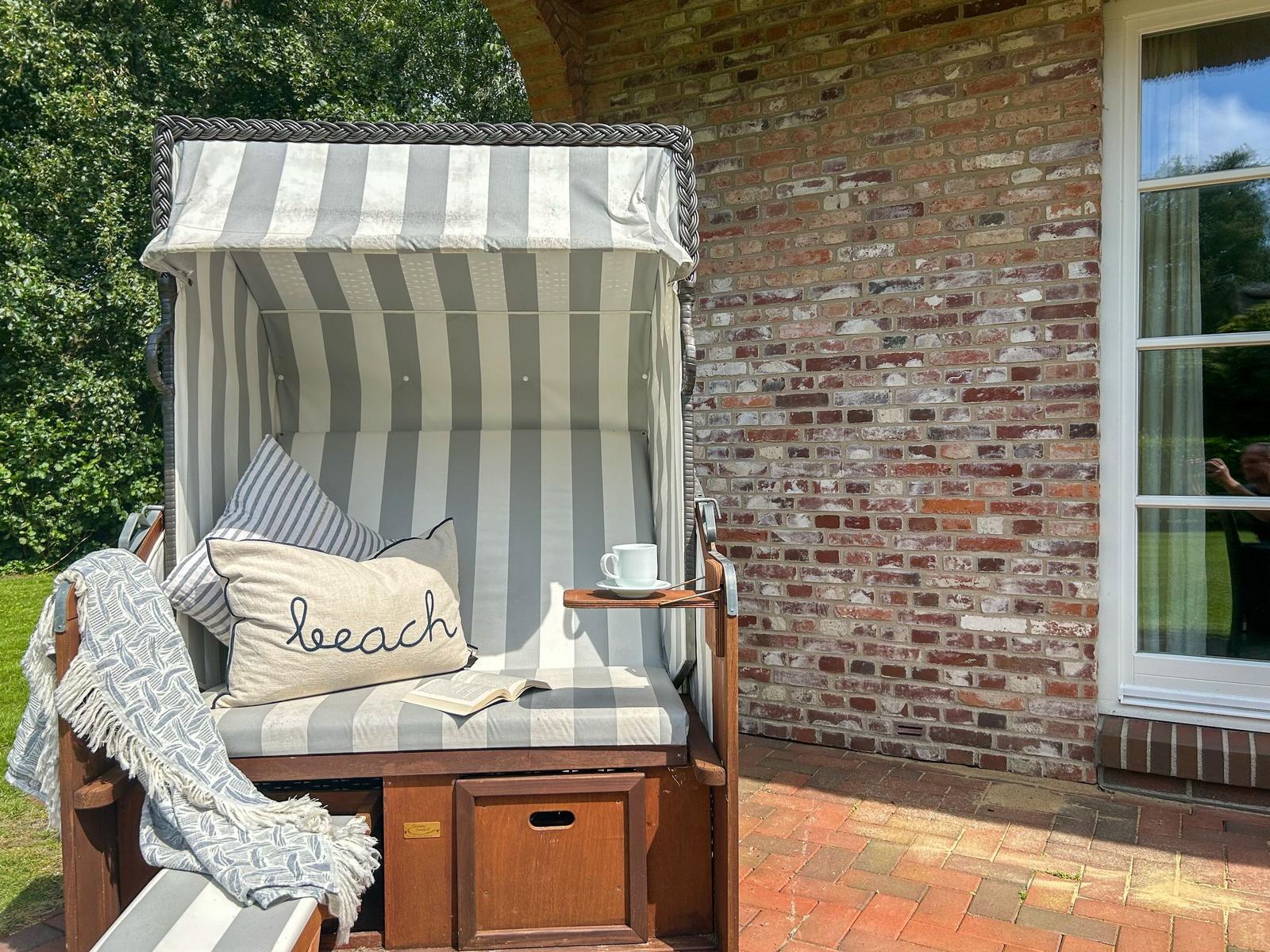 Strandkorb mit Kissen und Buch auf Terrasse neben Backsteinwand.