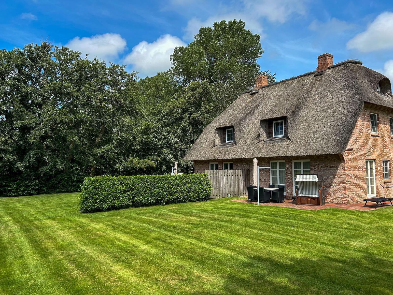 Haus mit strohgedecktem Dach, Garten und Terrasse mit Gartenmöbeln.