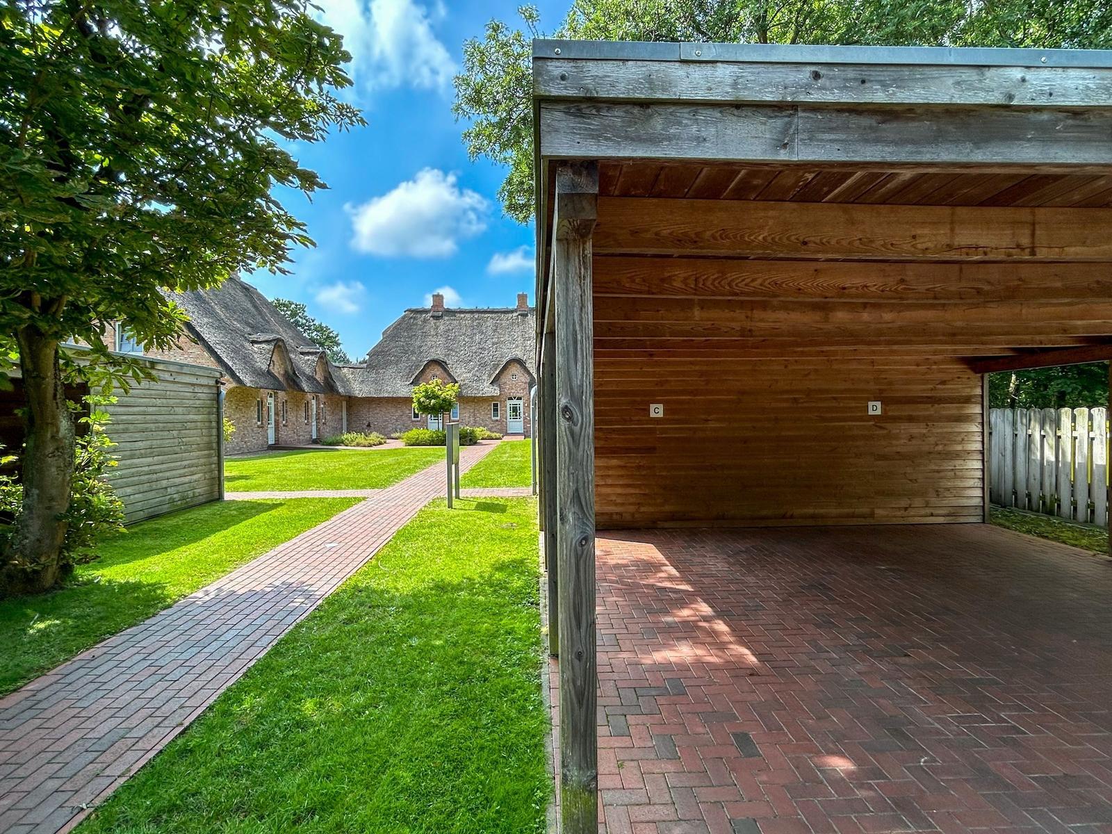 Holzüberdachter Bereich mit Blick auf traditionelle Dachhäuser und grünen Rasen.