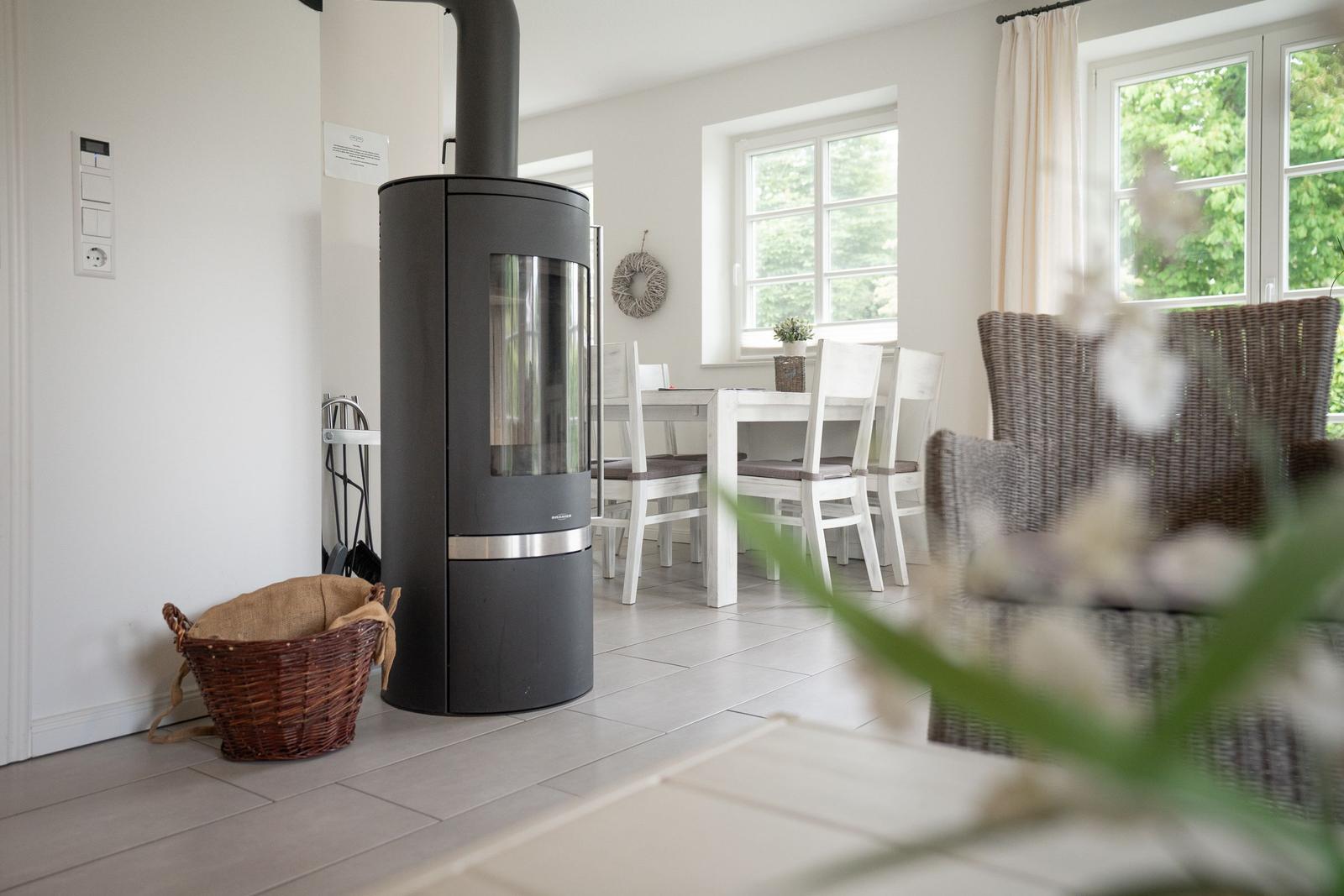 Wohn- und Essbereich mit Kaminofen, Tisch, Stühlen und Fenstern.