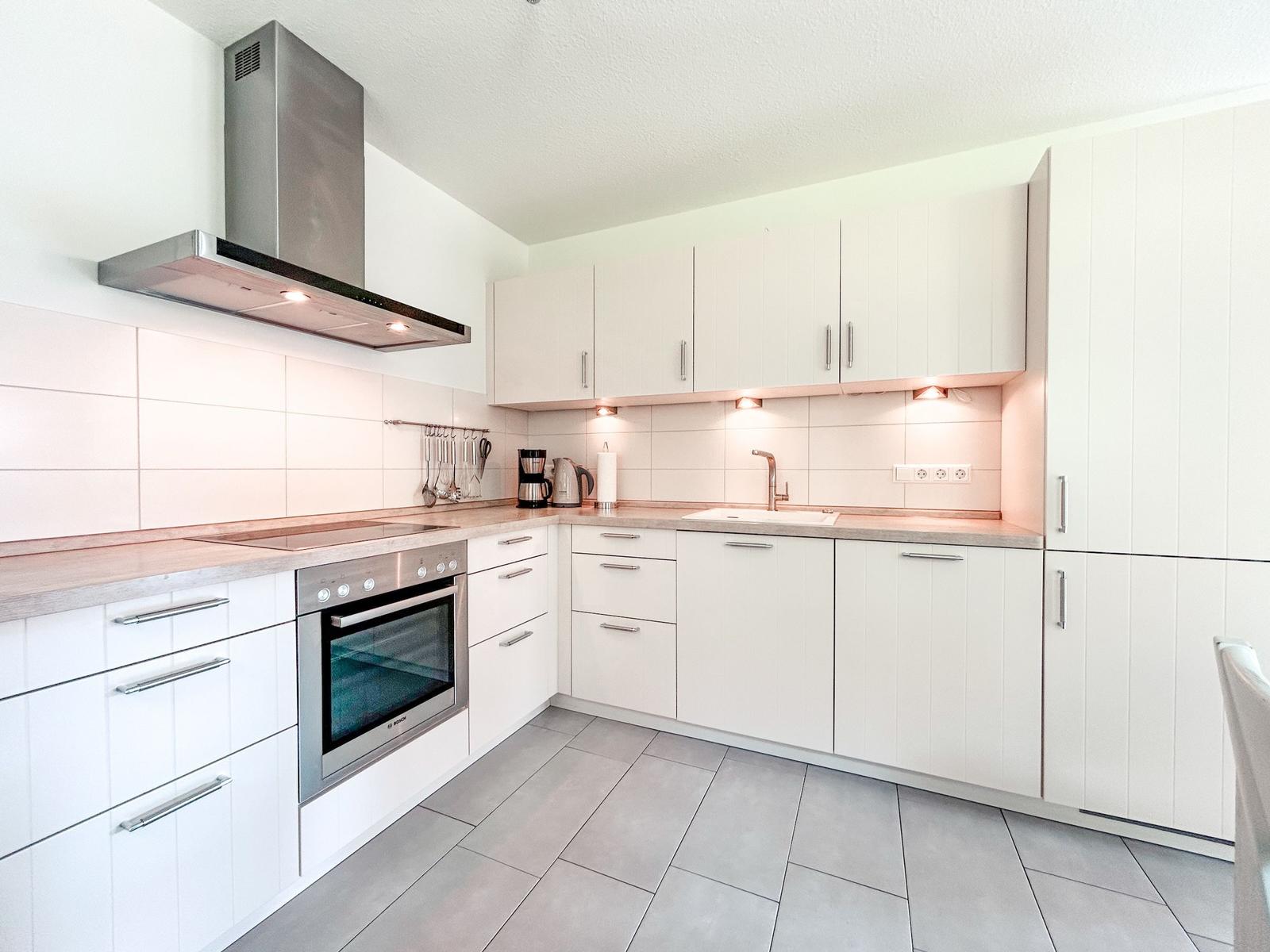 Moderne Küche mit weißen Schränken, Edelstahlgeräten und Holzoberflächen.