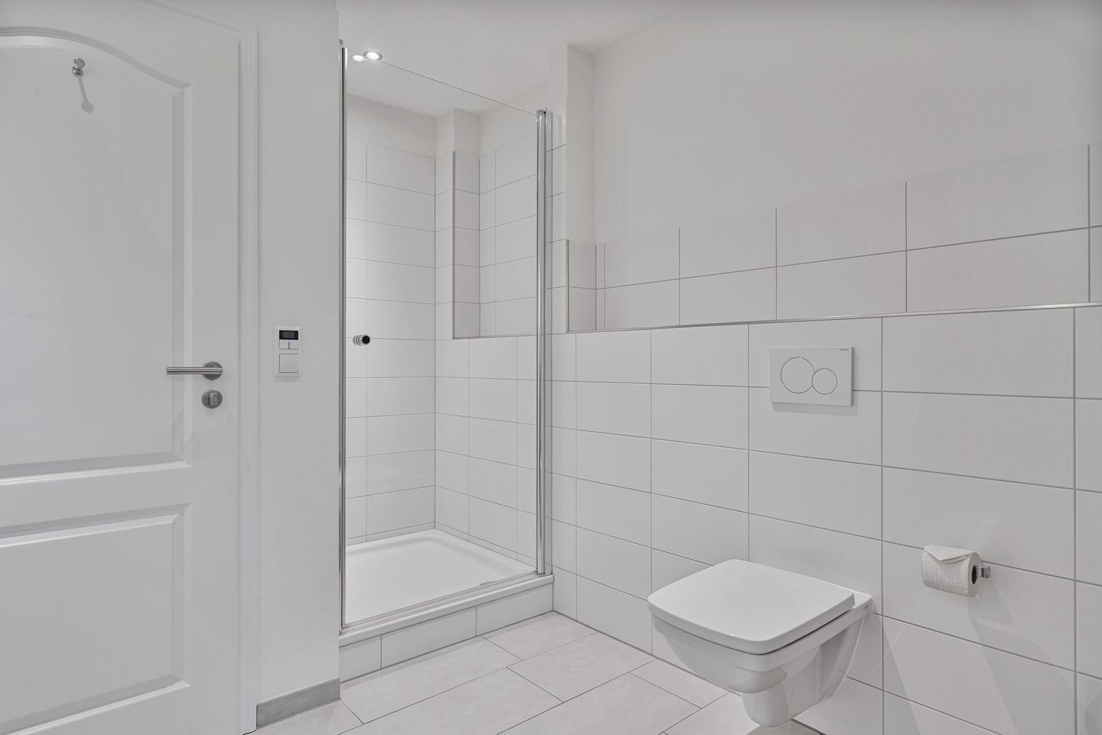 Badezimmer mit Dusche, Toilette und Toilettenpapierhalter.