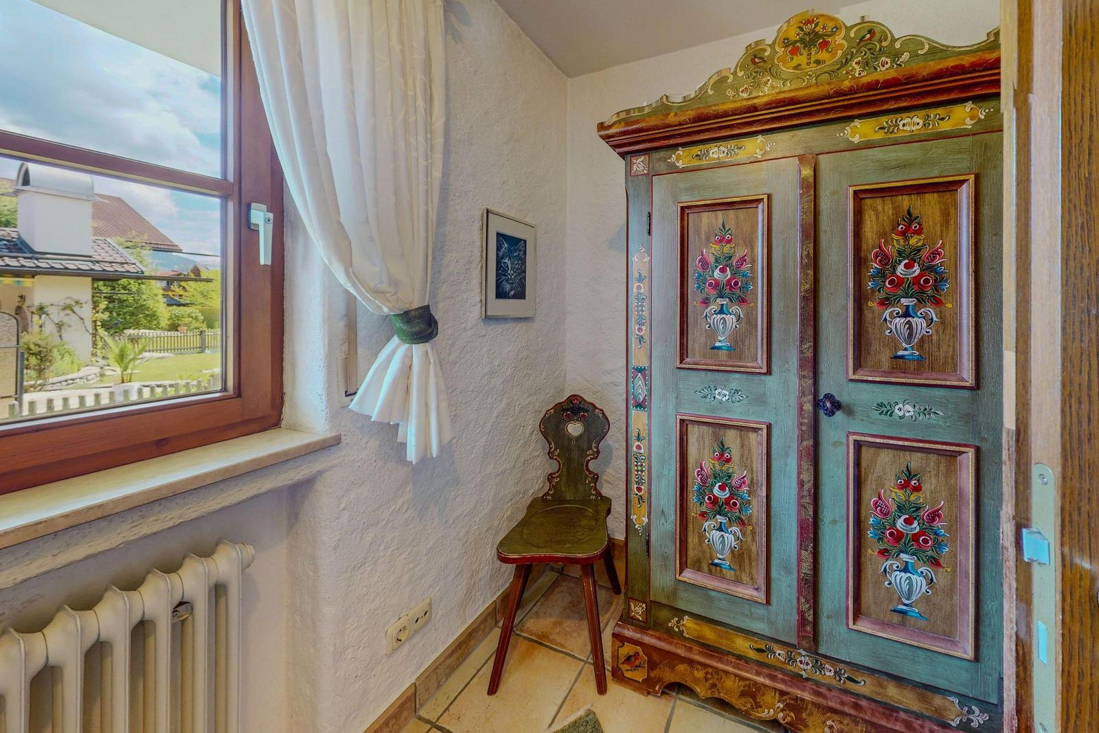 Ein Raum mit einem bemalten Schrank, einem Stuhl und einem Fenster mit Blick auf die Außenterrasse.