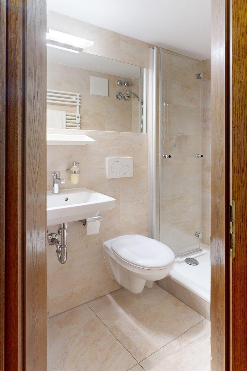 Badezimmer mit Dusche, Waschbecken und WC. Fliesen und Spiegel sichtbar.