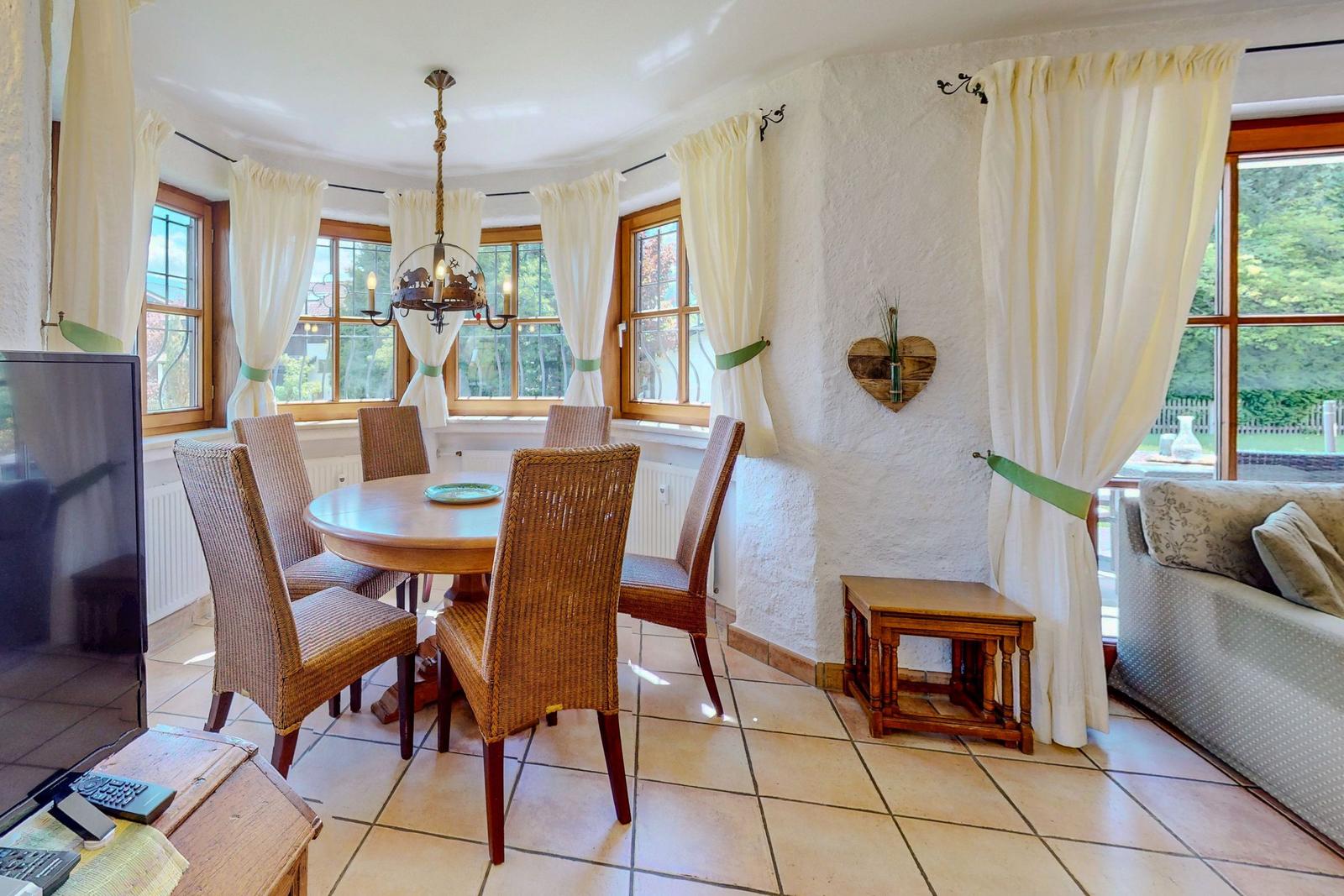 Esszimmer mit runden Tisch, Stühlen und Fenstern mit weißen Vorhängen.