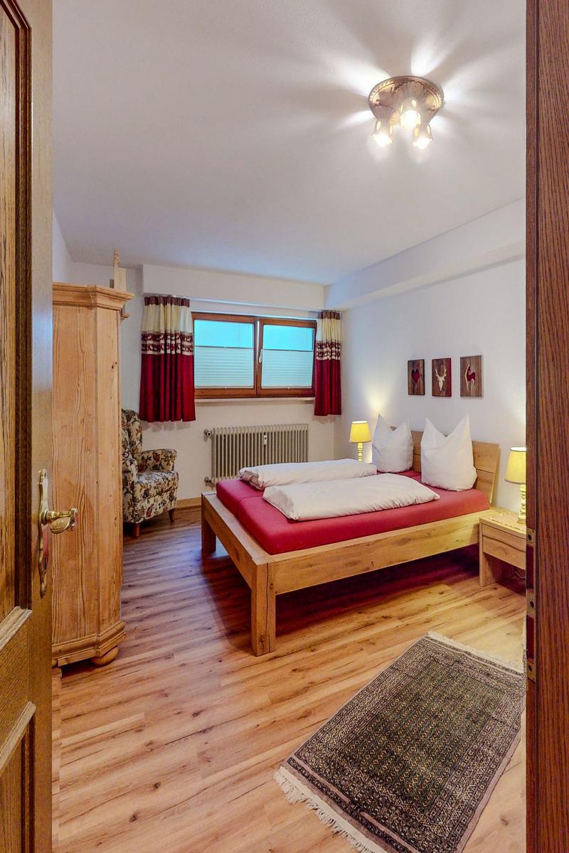 Schlafzimmer mit Holzbett, Kleiderschrank und Fenster mit Vorhängen.