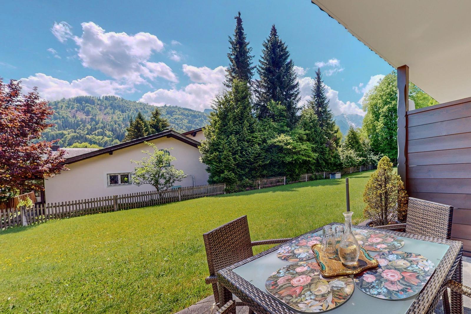 Terrasse mit Tisch und Stühlen, Blick auf grünen Garten und Berge.