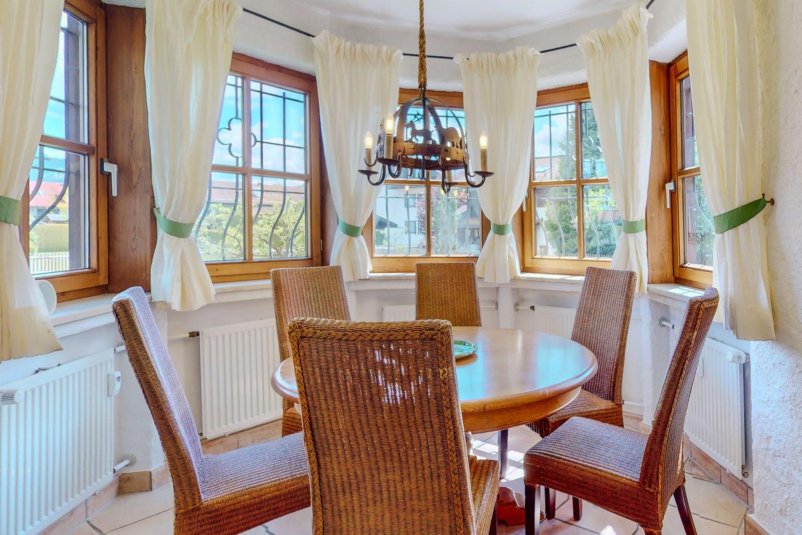 Runder Esstisch mit sechs Stühlen in einem Raum mit Fenstern und Vorhängen.