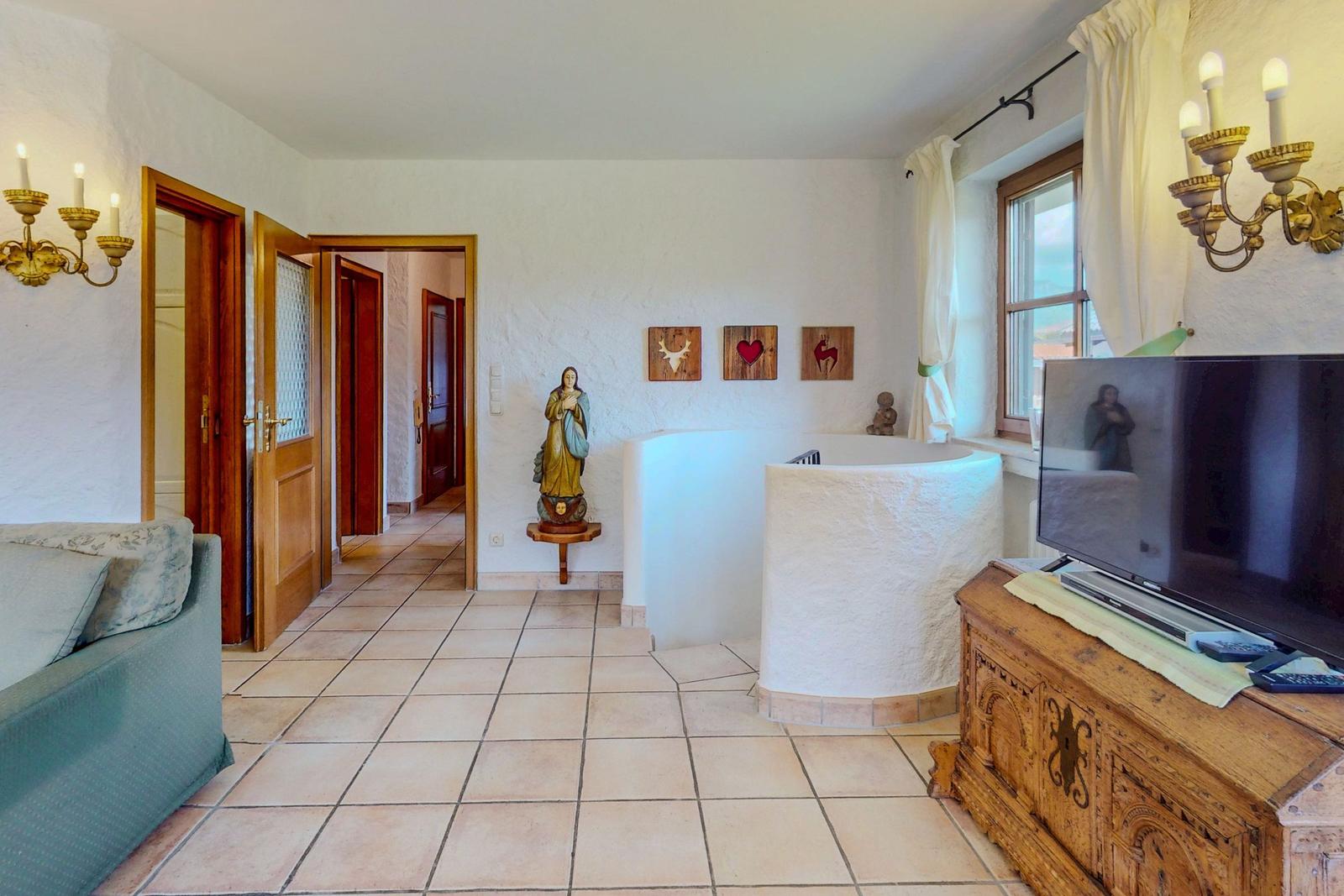 Wohnraum mit Badewanne, TV und Holzmöbel. Türöffnungen führen in andere Räume.