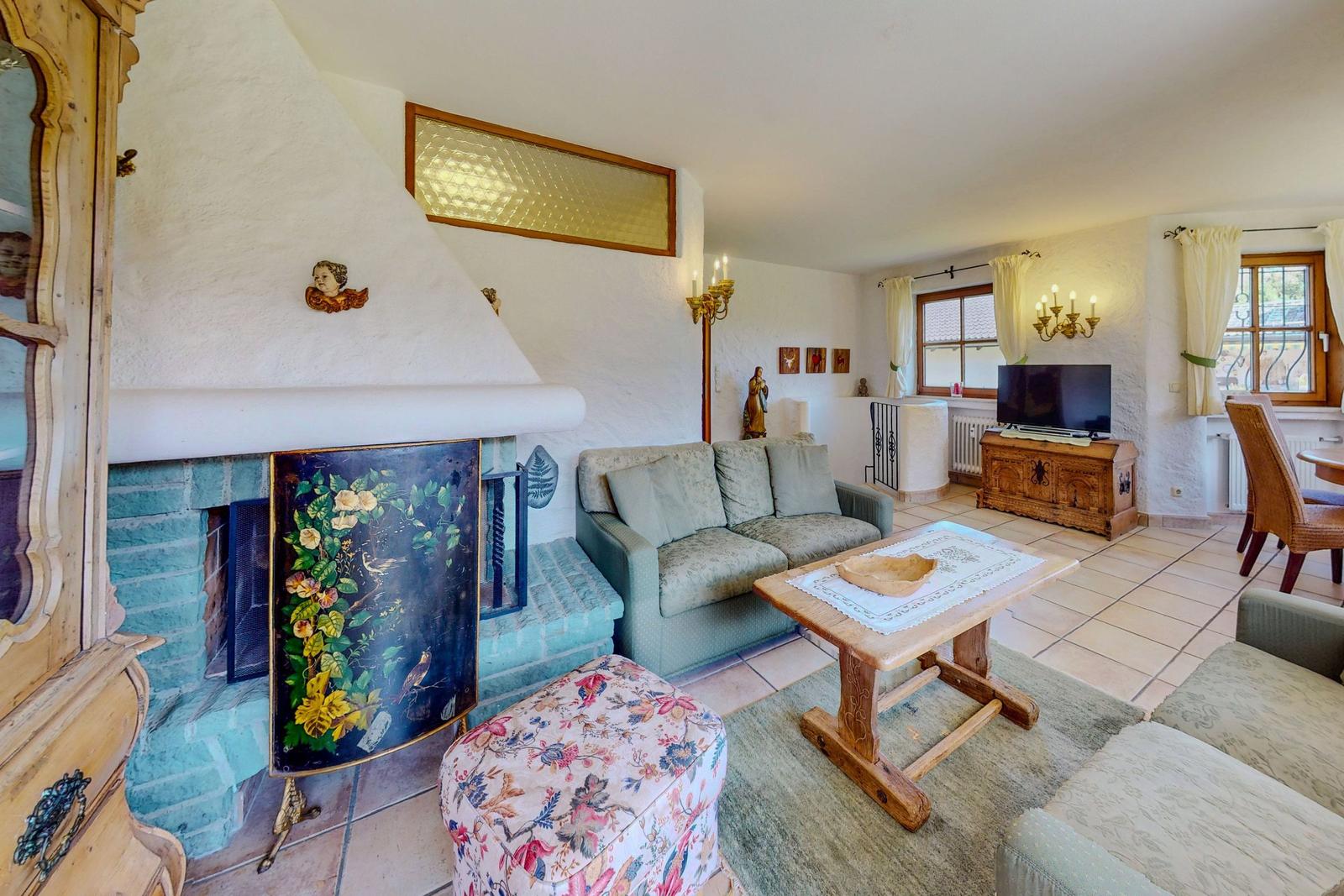 Wohnzimmer mit Kamin, Sofa, Tisch und TV. Holzmöbel und Fenster mit Vorhängen.