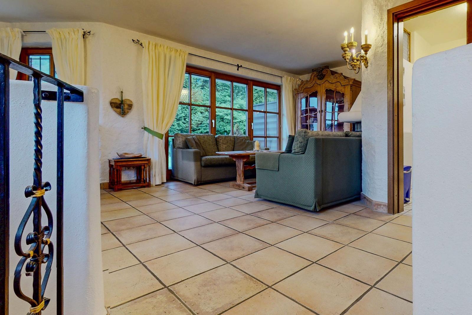 Wohnzimmer mit Sofa, Tisch und Fenstern. Holzgeländer und Kronleuchter sichtbar.