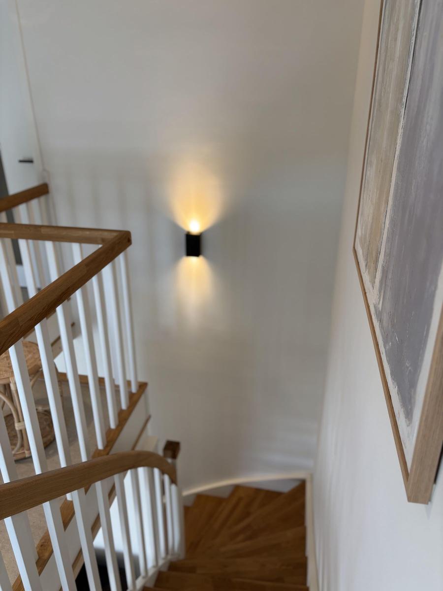 Haus mit Holztreppe und Wandbeleuchtung. Bild zeigt Treppenhaus mit Kunstwerk.