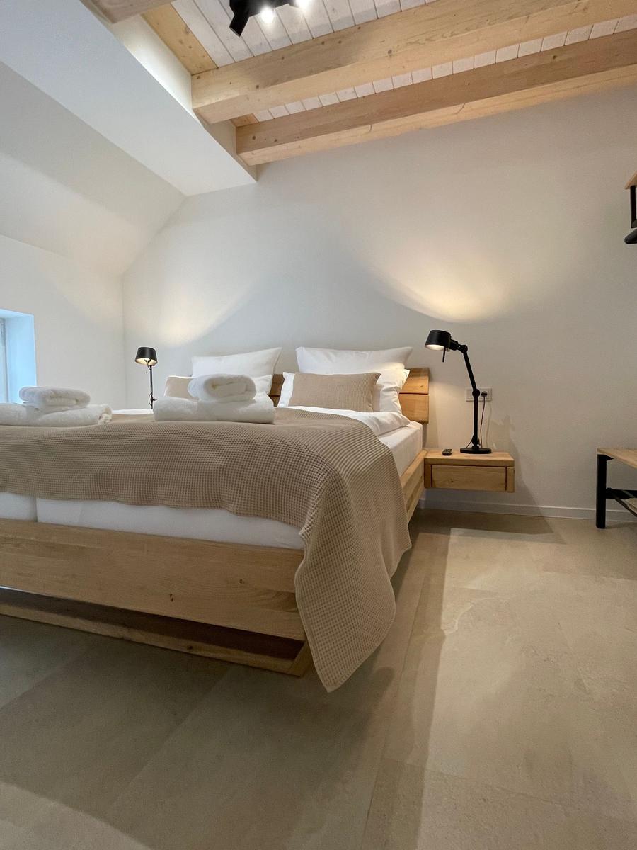 Schlafzimmer mit Holzbett, Nachttisch und Decke. Holzbalken an der Decke.