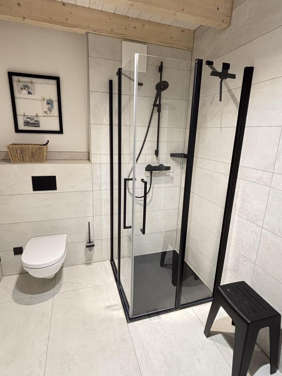 Dusche mit Glaswand, Toilette und schwarzer Sitzbank