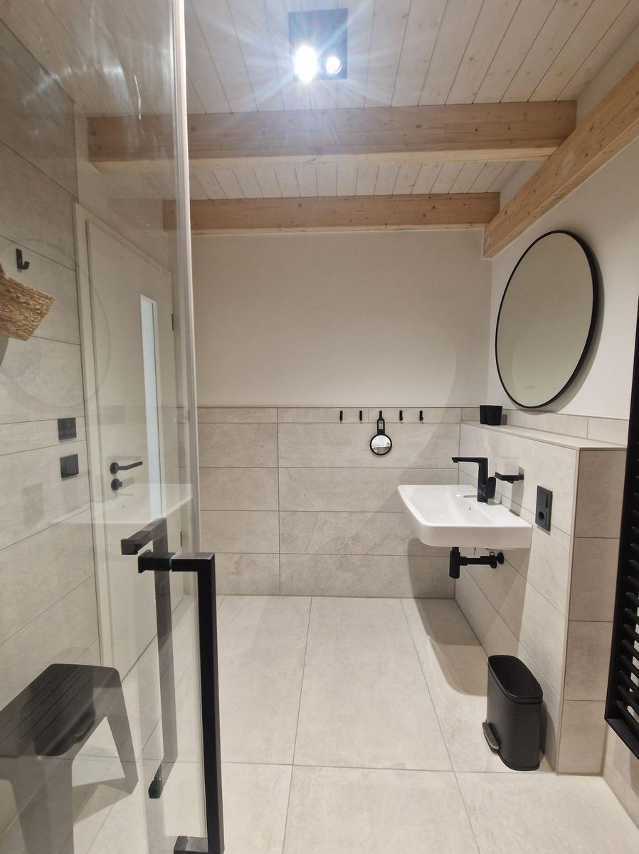 Bad mit Dusche, Waschbecken und runden Spiegel an der Wand.