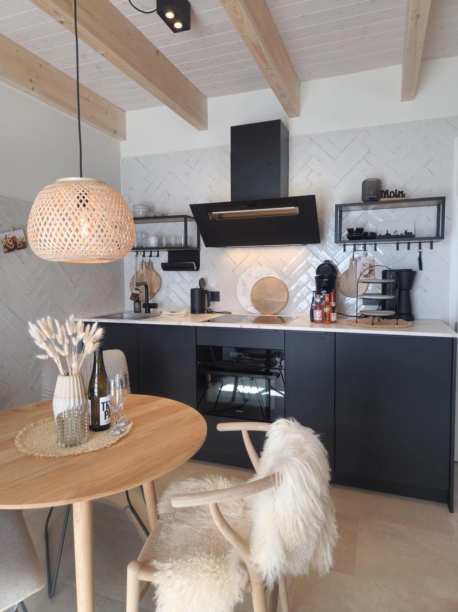 Küche mit Essbereich, schwarze Schränke, helle Fliesenwand und Holzbalkendecke.