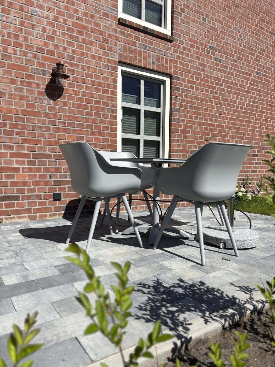 Terrasse mit grauem Tisch und Stühlen vor rotem Backsteinhaus