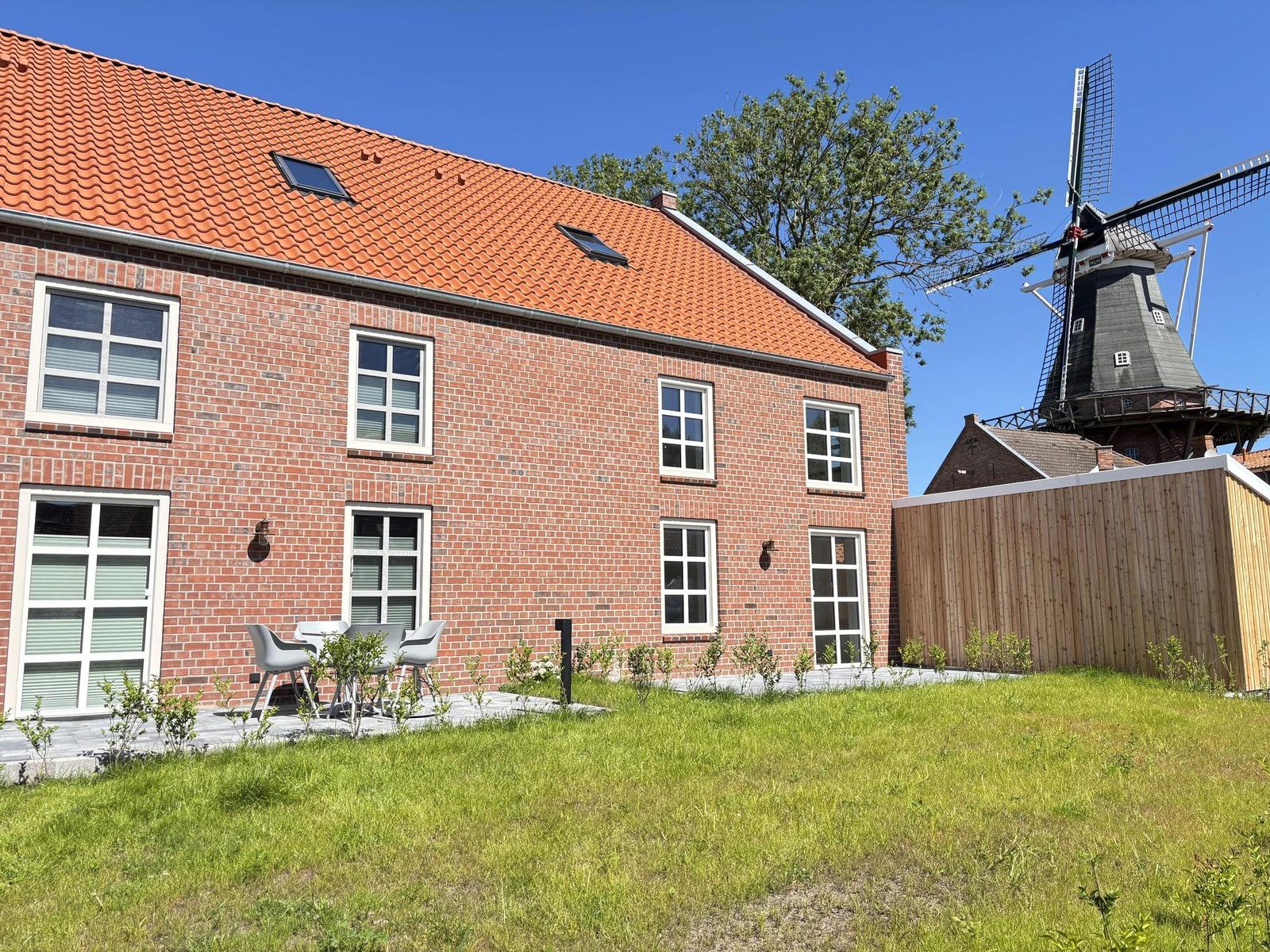 Rotes Ziegelhaus mit Terrasse und Windmühle im Hintergrund.