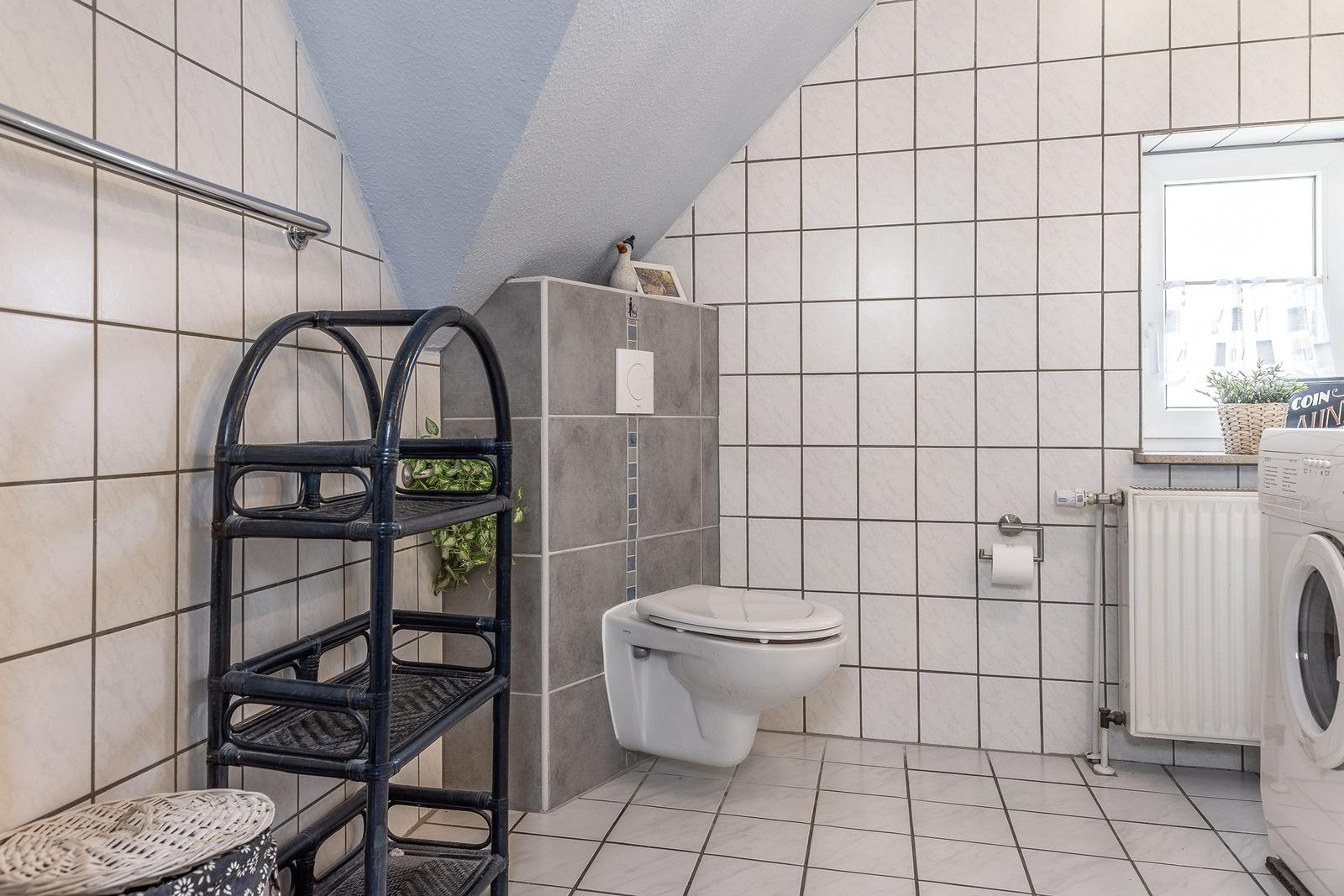 Badezimmer mit Toilette, Waschmaschine und Regal. Dachneigung und Fenster sichtbar.