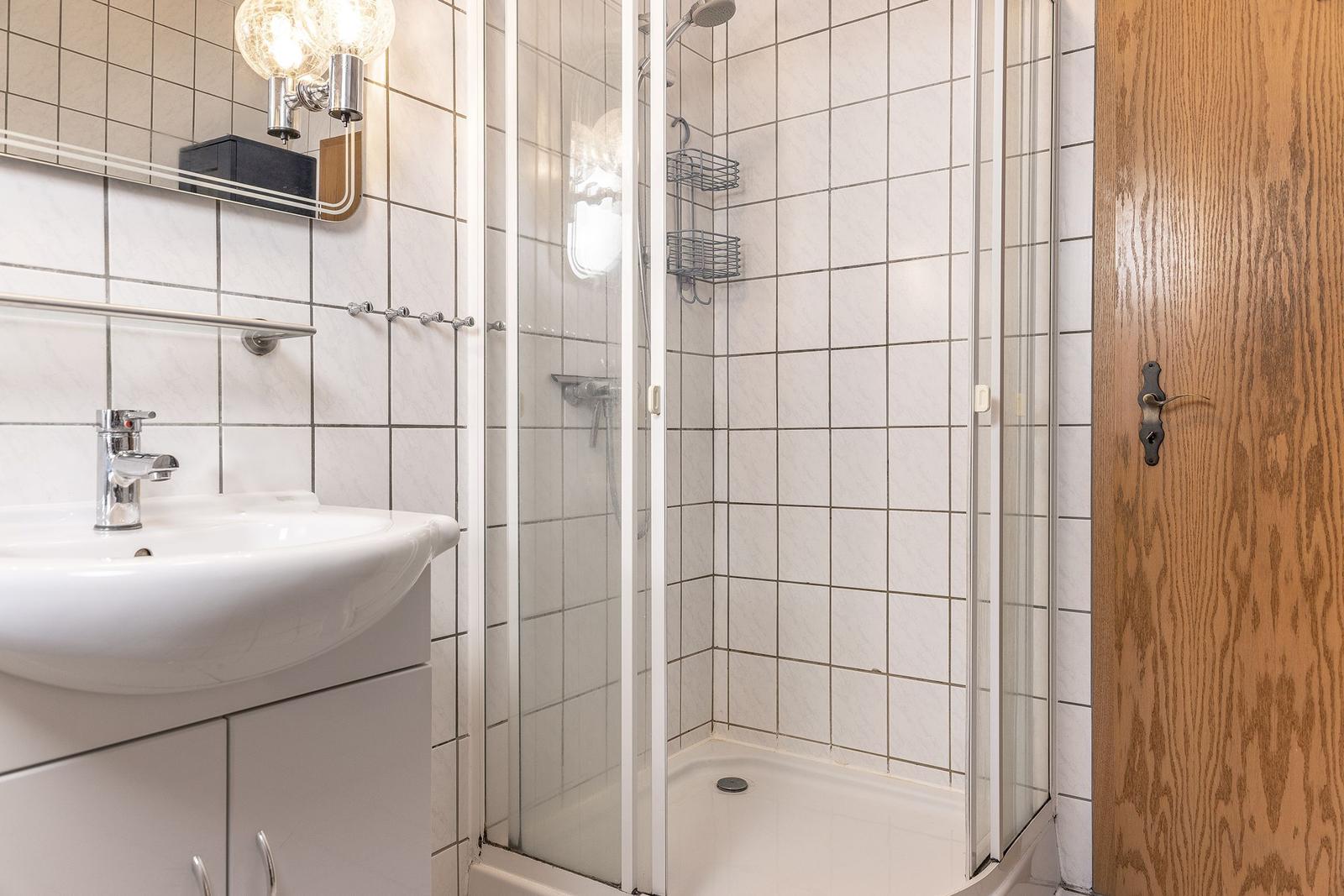 Badezimmer mit Dusche, Waschbecken und Spiegel.