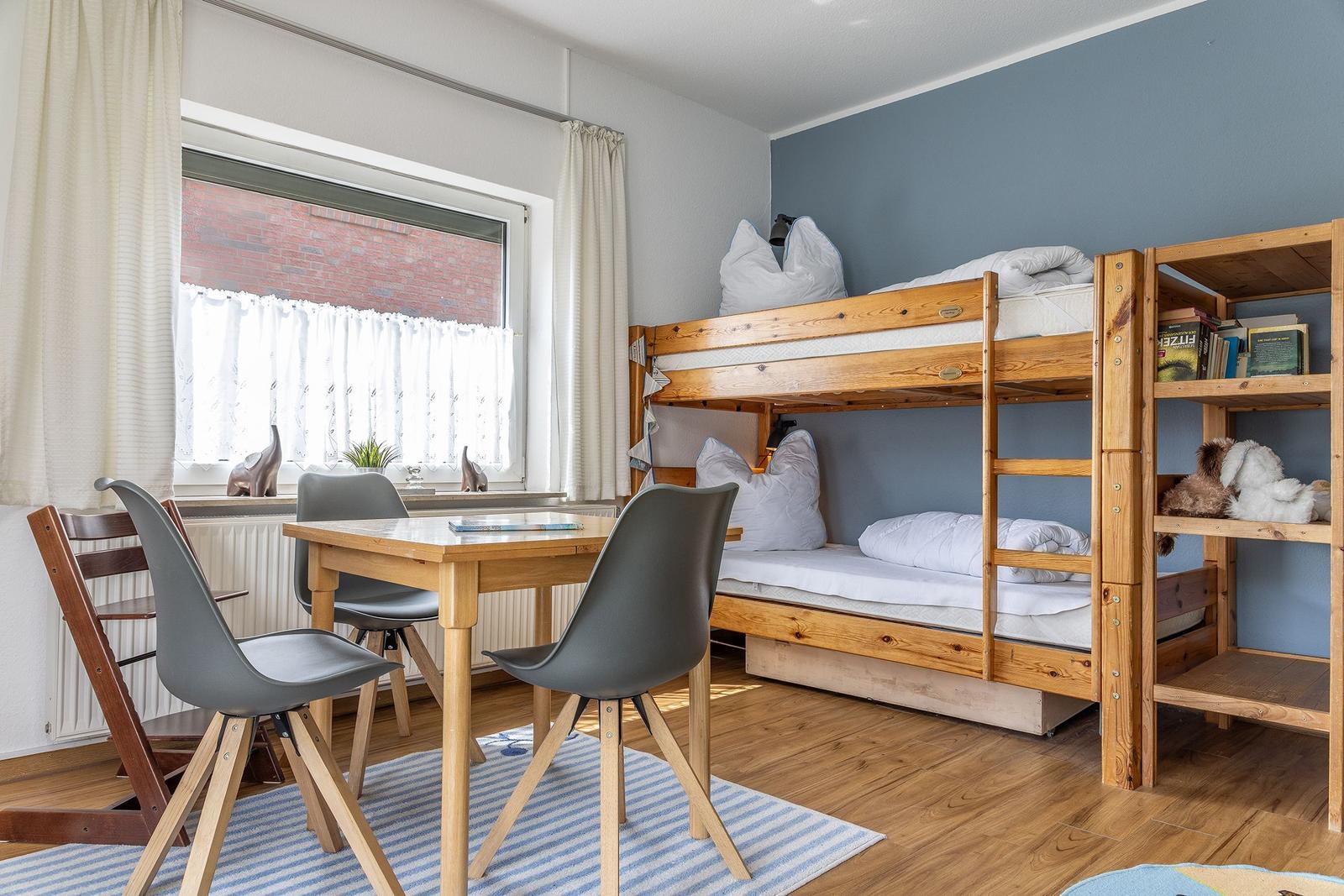 Ein Raum mit Schlafcouch, Tisch und Stühlen. Fenster mit Vorhängen.