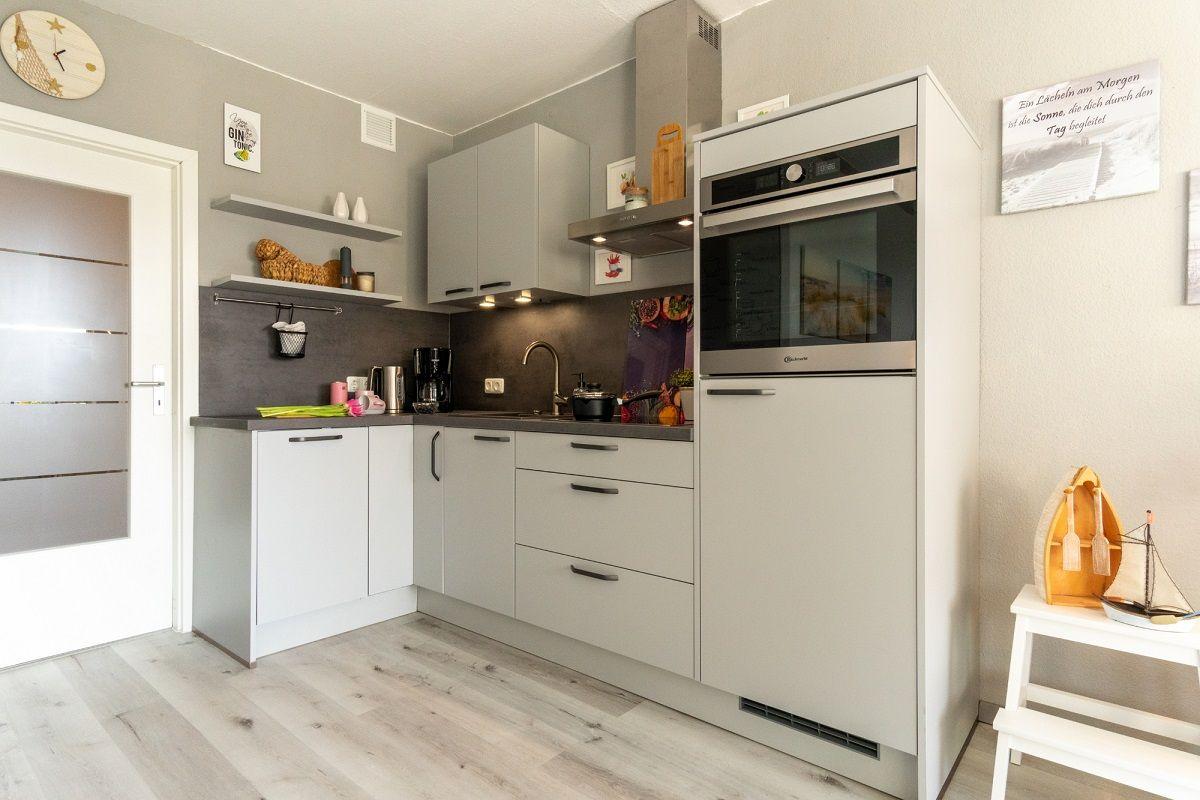 Küche mit grauen Schränken, Edelstahl-Küchenzeile und Holzboden.