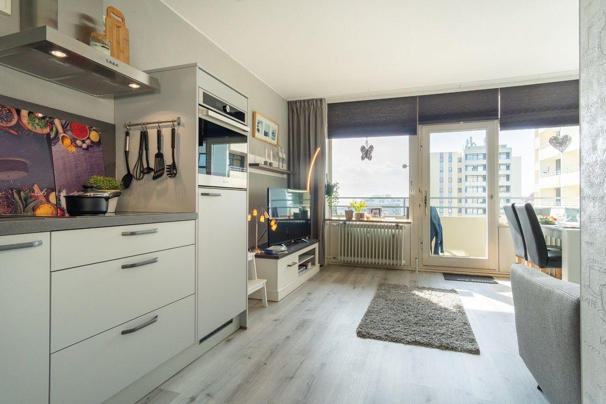 Küche mit Wohnbereich und Balkon mit Blick auf Hochhäuser.