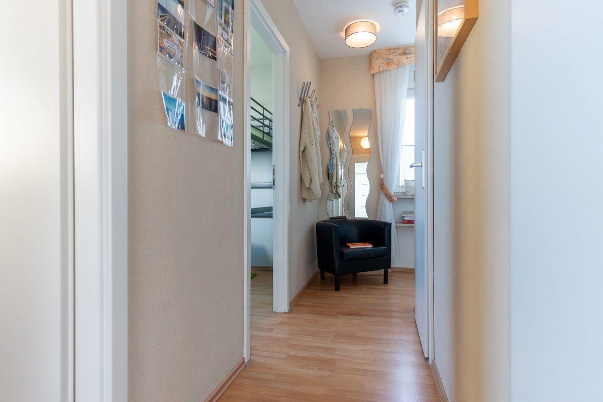 Flur mit Holzboden, schwarzer Sitzgelegenheit und Spiegel an der Wand.