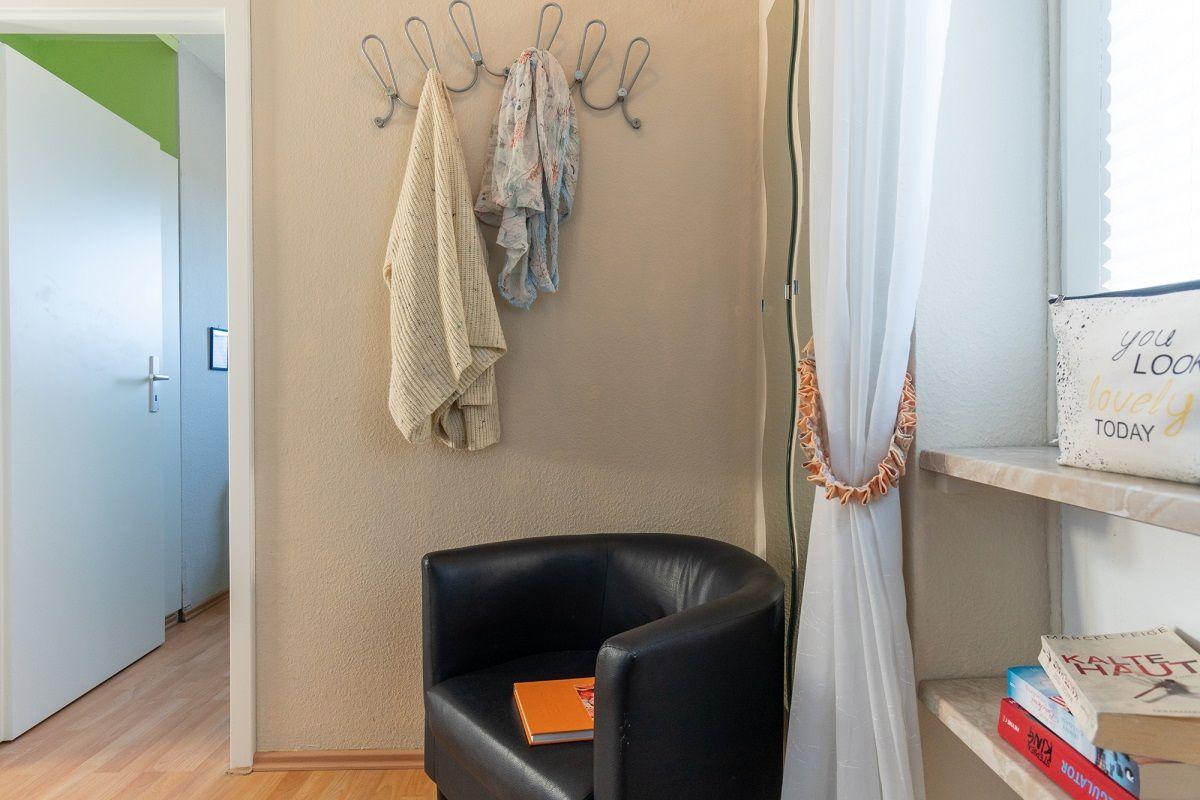 Schwarzer Sessel neben Fenster mit Bücherregal und Haken an Wand.