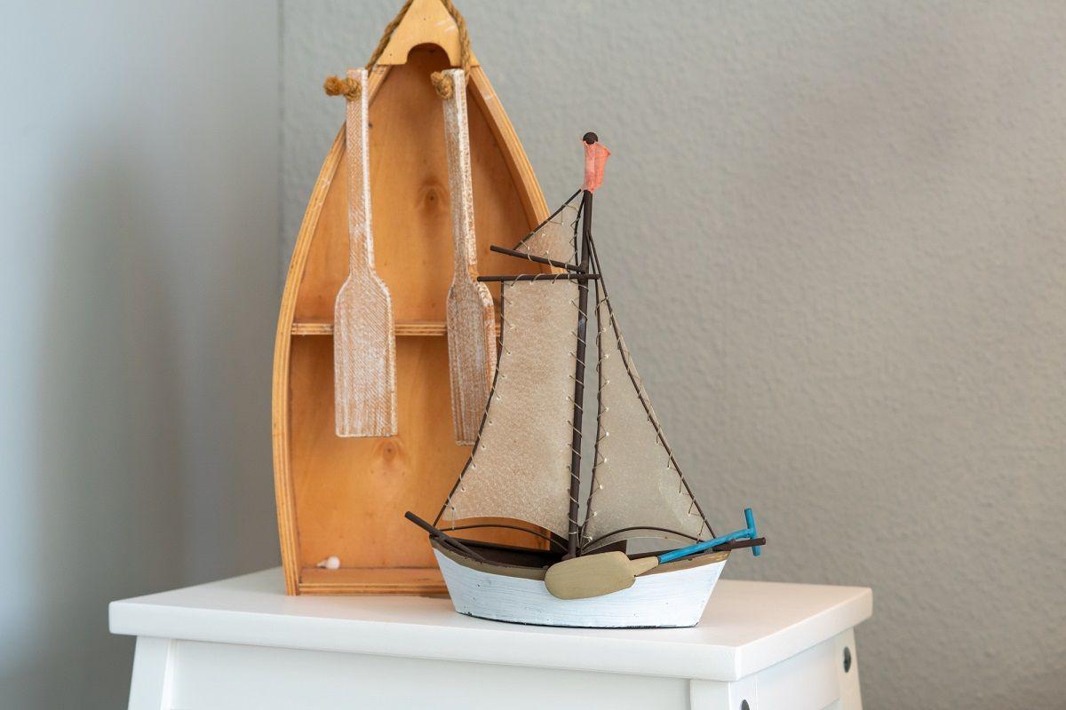 Ein hölzernes Bootmodell mit Rudern und Segeln steht auf einem weißen Tisch.