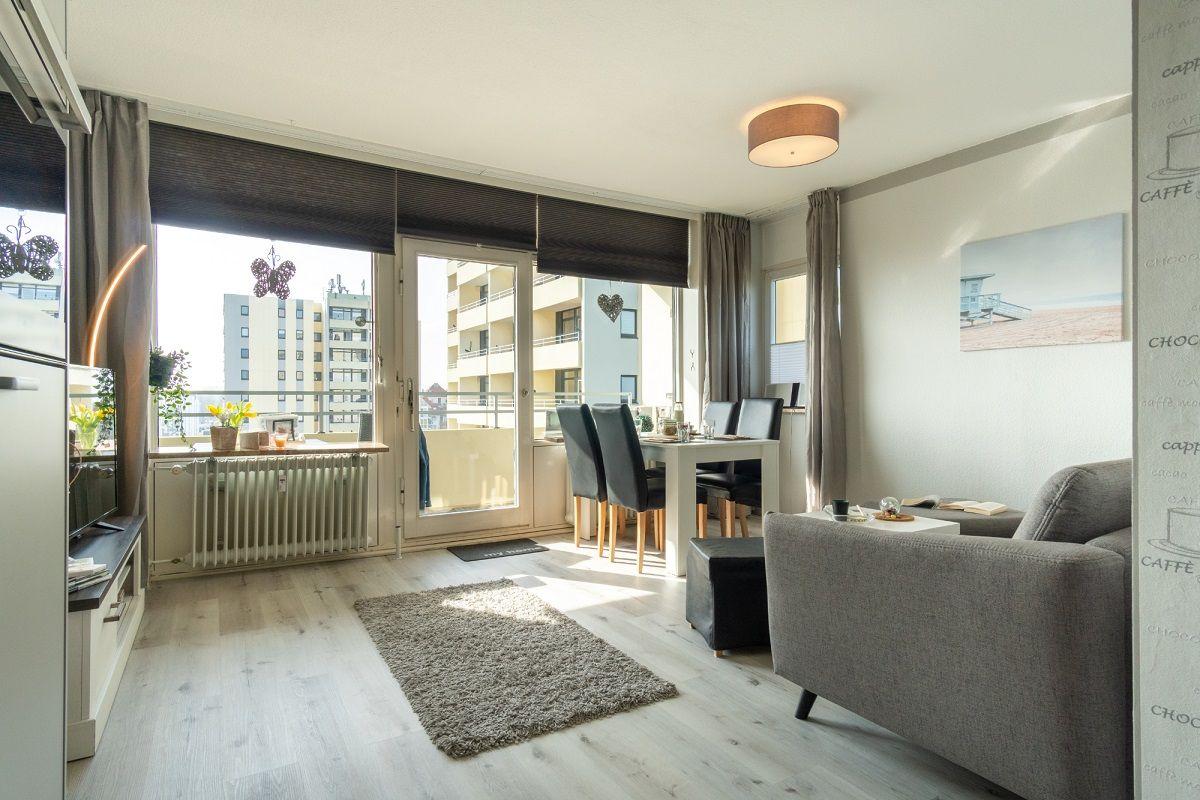 Wohnung mit Essbereich, Sofa und Balkon. Holzboden und Fensterfront.