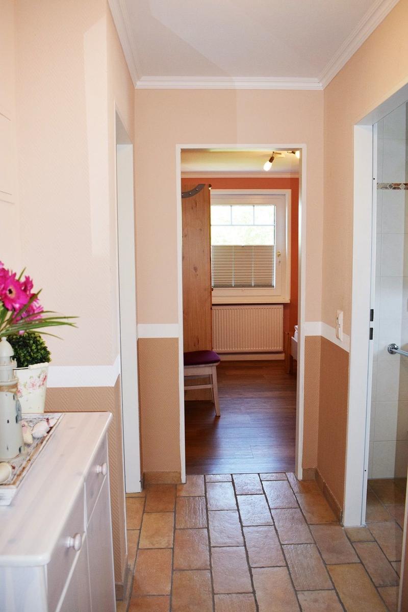 Flur mit Terrakottaboden, Tür zu Schlafzimmer und Bad. Links Küchenzeile mit Blumen.