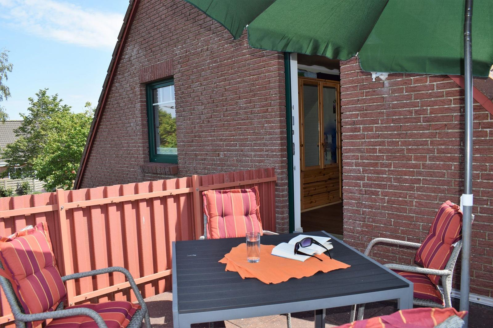 Terrasse mit Tisch, Stühlen und Sonnenschirm neben Backsteinhaus