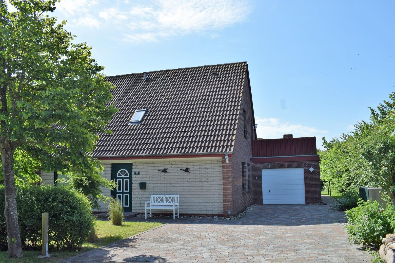 Ein Haus mit Garage, weiße Bank und grüner Umgebung.