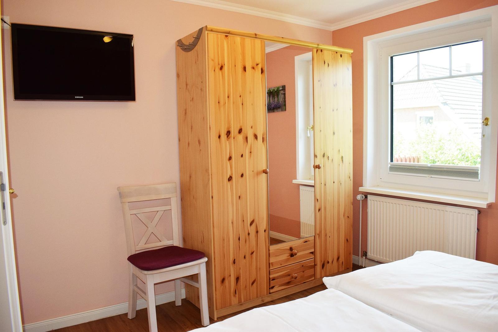 Schlafzimmer mit Bett, Kleiderschrank, Stuhl und Fernseher an der Wand.