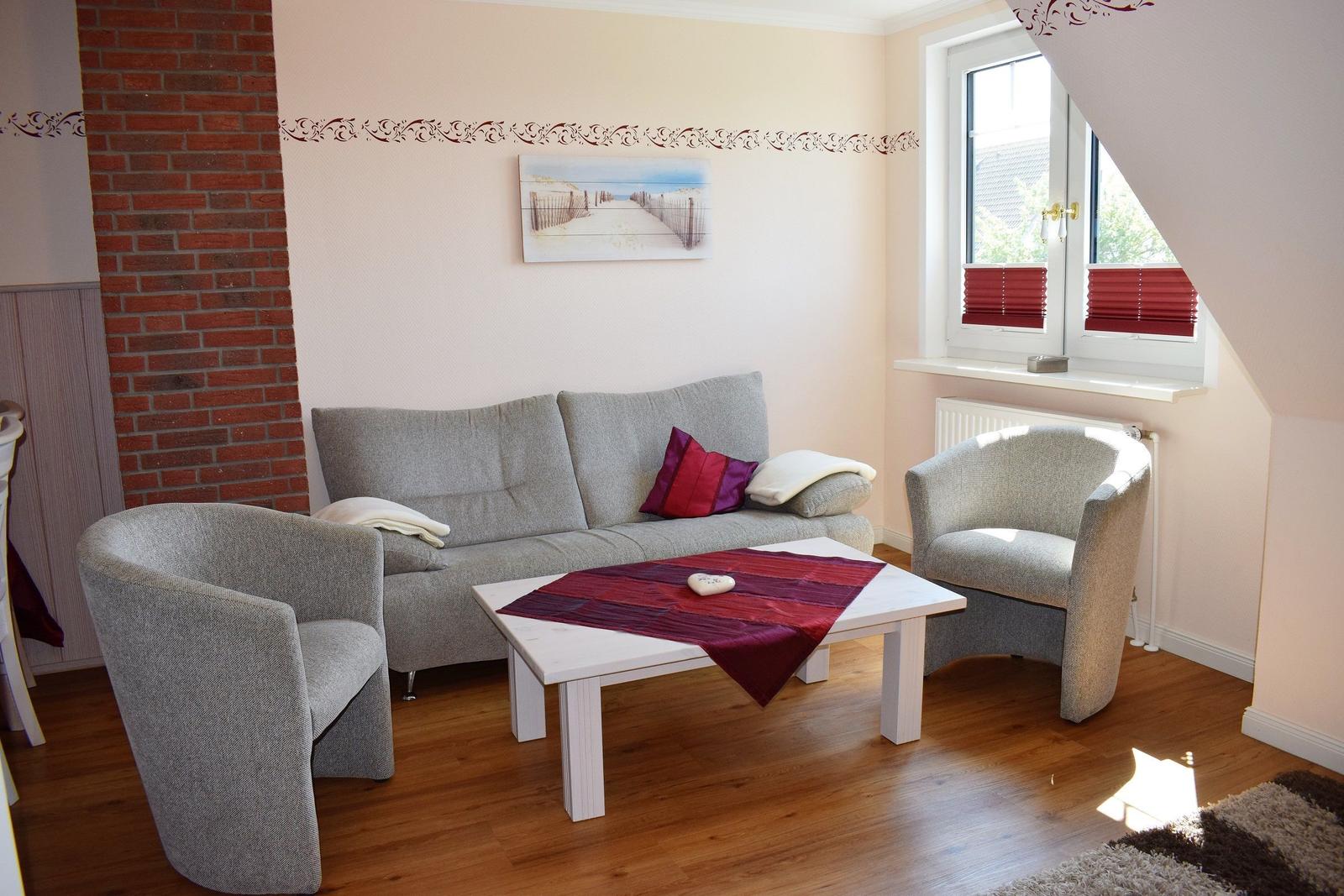 Wohnzimmer mit Sofa, zwei Sesseln und Tisch. Fenster mit roten Jalousien.