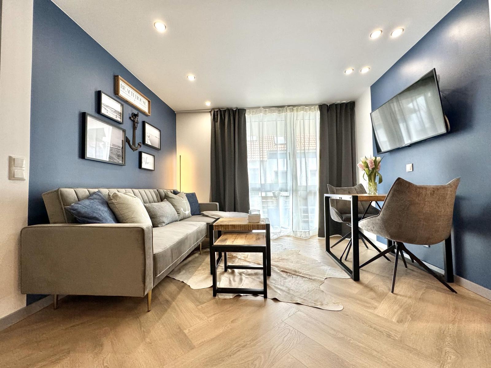 Wohnbereich mit Sofa, Esstisch und TV an blauen Wänden.