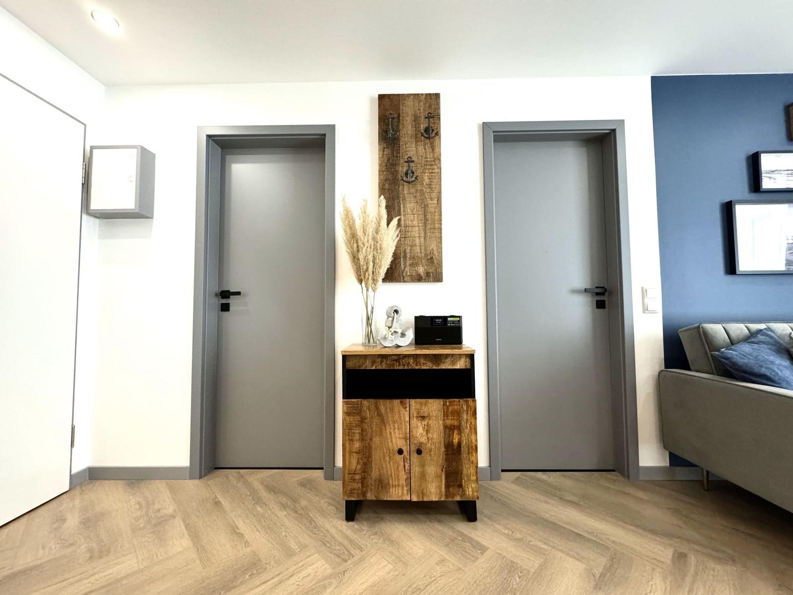 Eingangsbereich mit Holzschrank, zwei Türen und blauer Wand im Hintergrund.