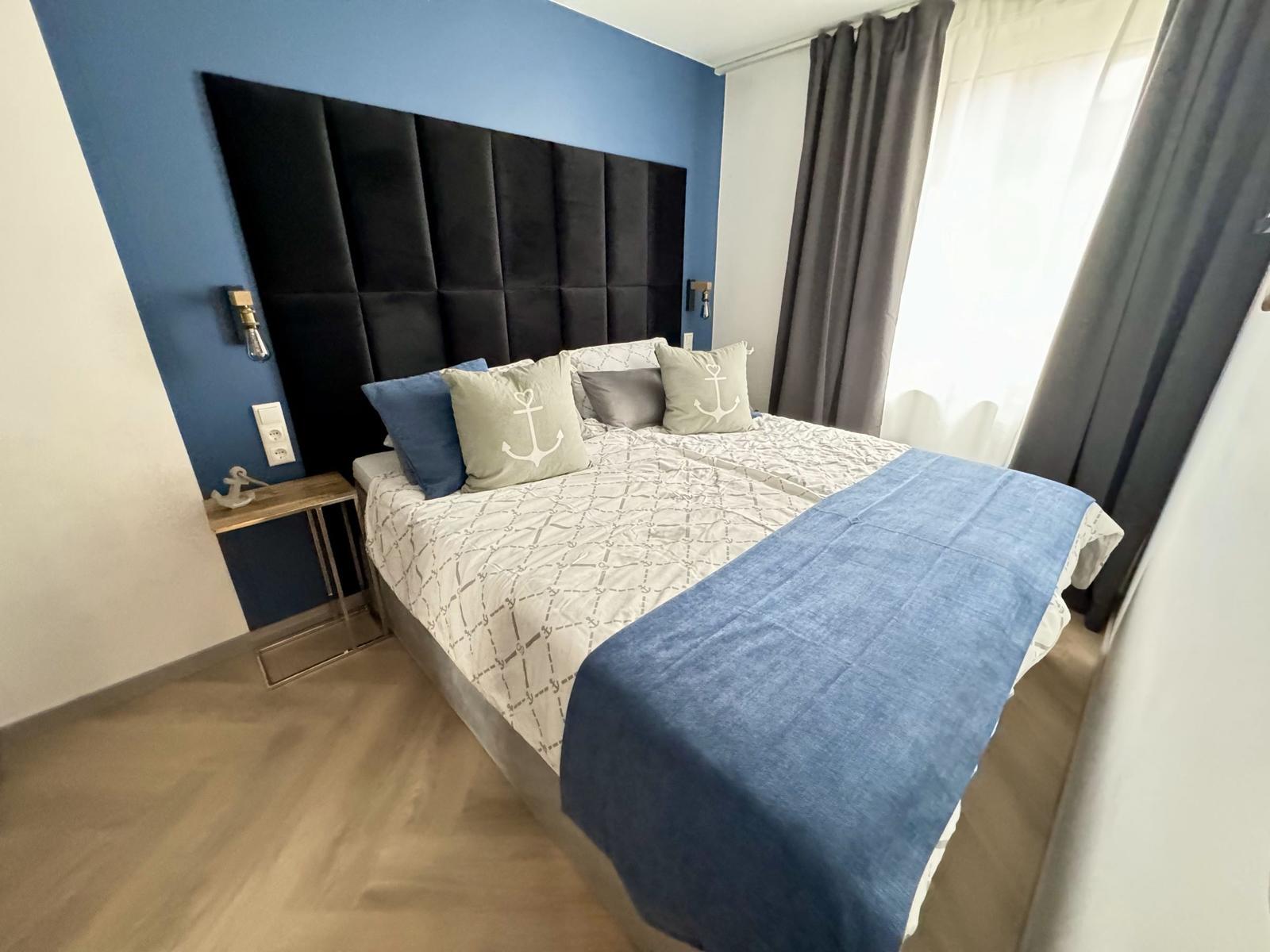 Schlafzimmer mit Bett, blauer Wand und Vorhängen.