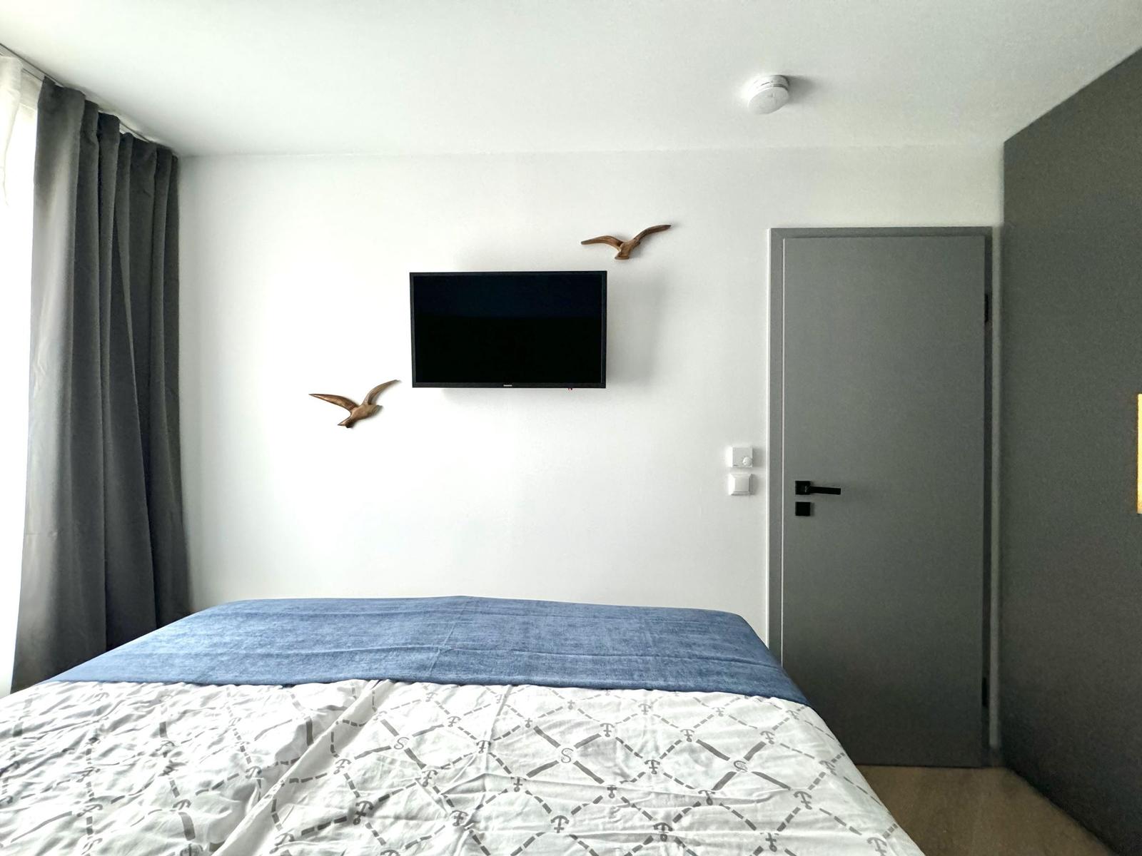 Schlafzimmer mit Bett, Wand-TV und Vogelskulpturen.
