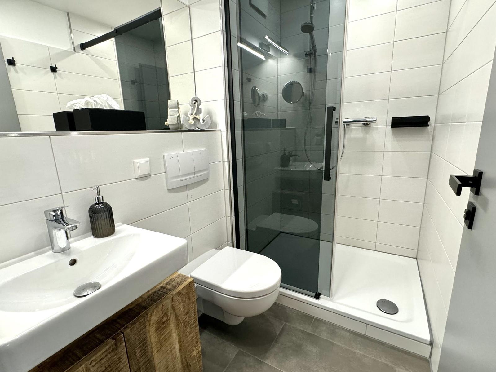 Badezimmer mit Dusche, Toilette und Waschbecken mit Spiegel.