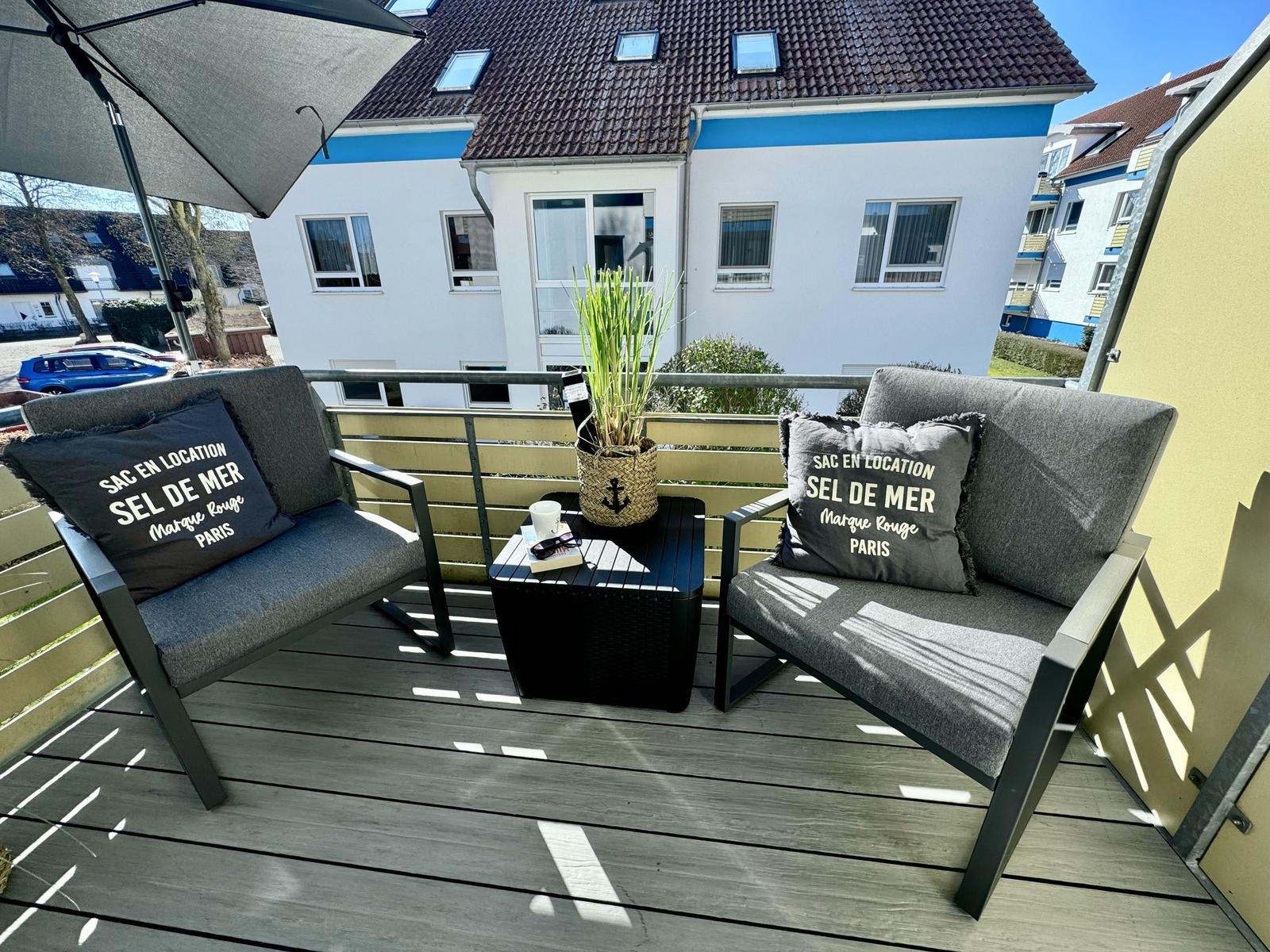 Terrasse mit zwei Sesseln, Tisch und Sonnenschirm. Blick auf Wohnhaus.